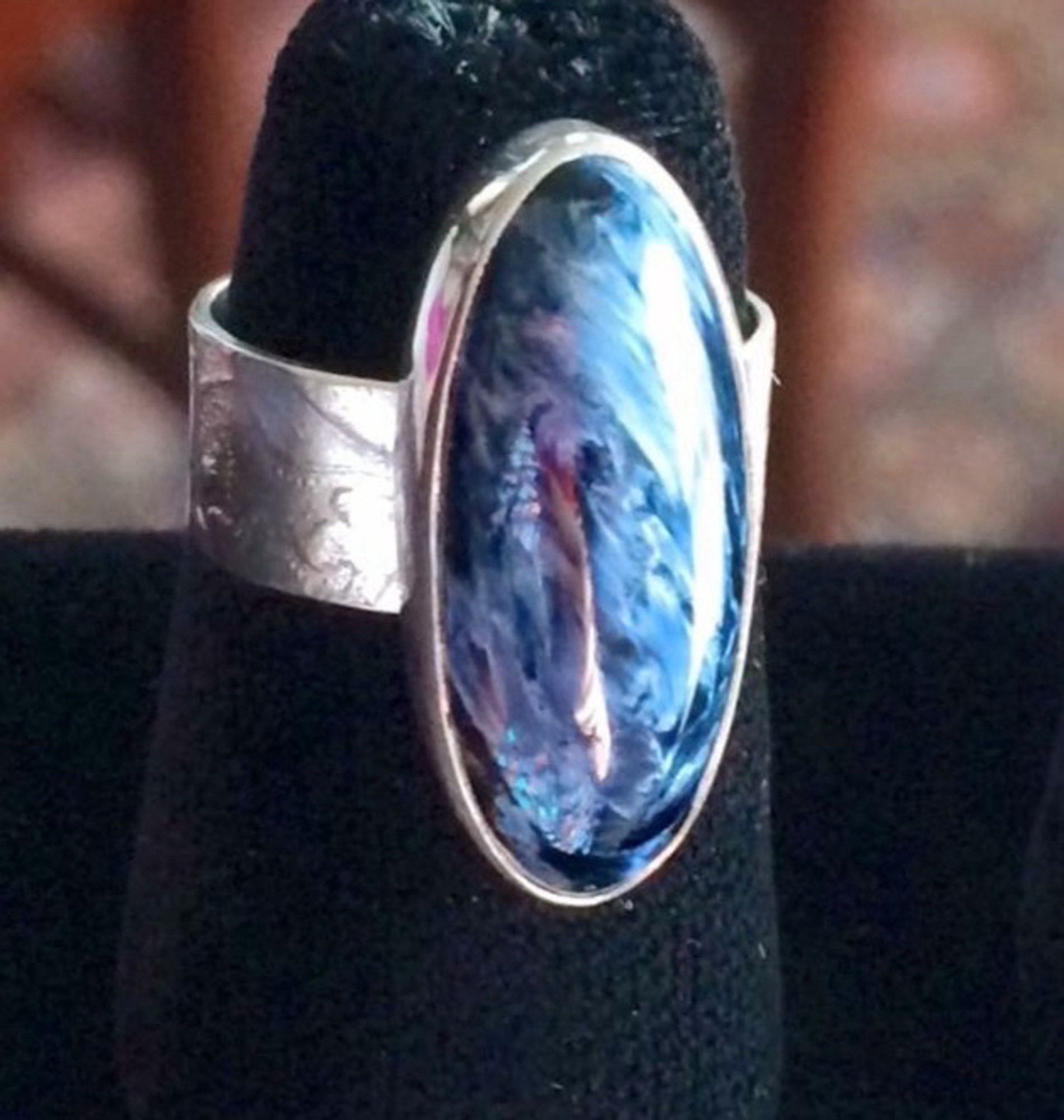 A ring with a wide band with Jacobean imprints on it. The sizable blue stone has many swirls all over it. The stone is a Namibian Pietersite, and is fairly rare outside of Namibia.