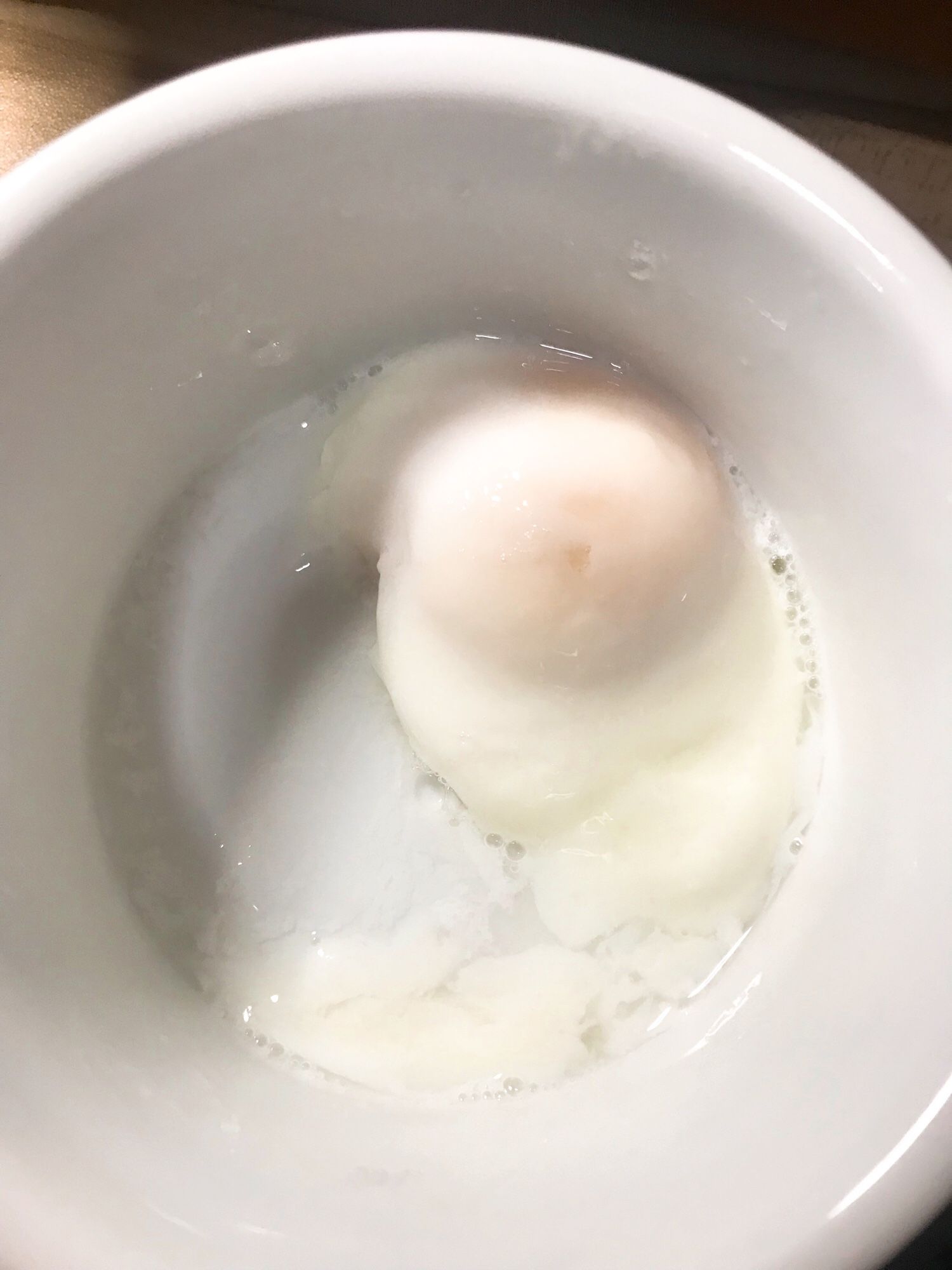 Closeup shot of a poached egg inside a white ramekin