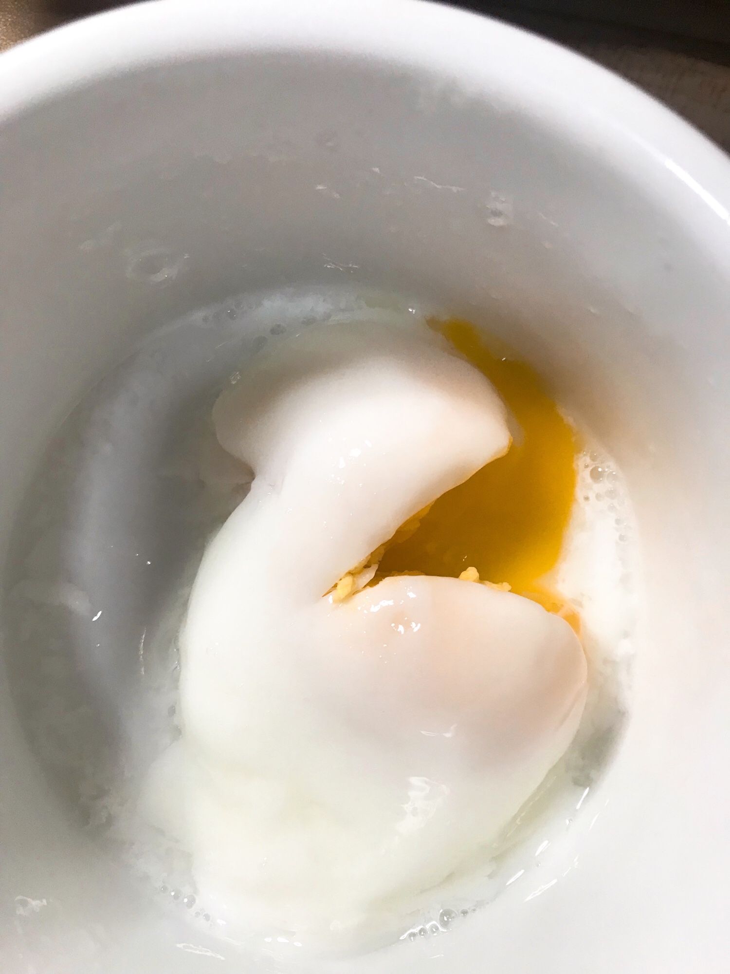 Closeup shot of a poached egg inside a white ramekin, the egg split to show a runny yolk