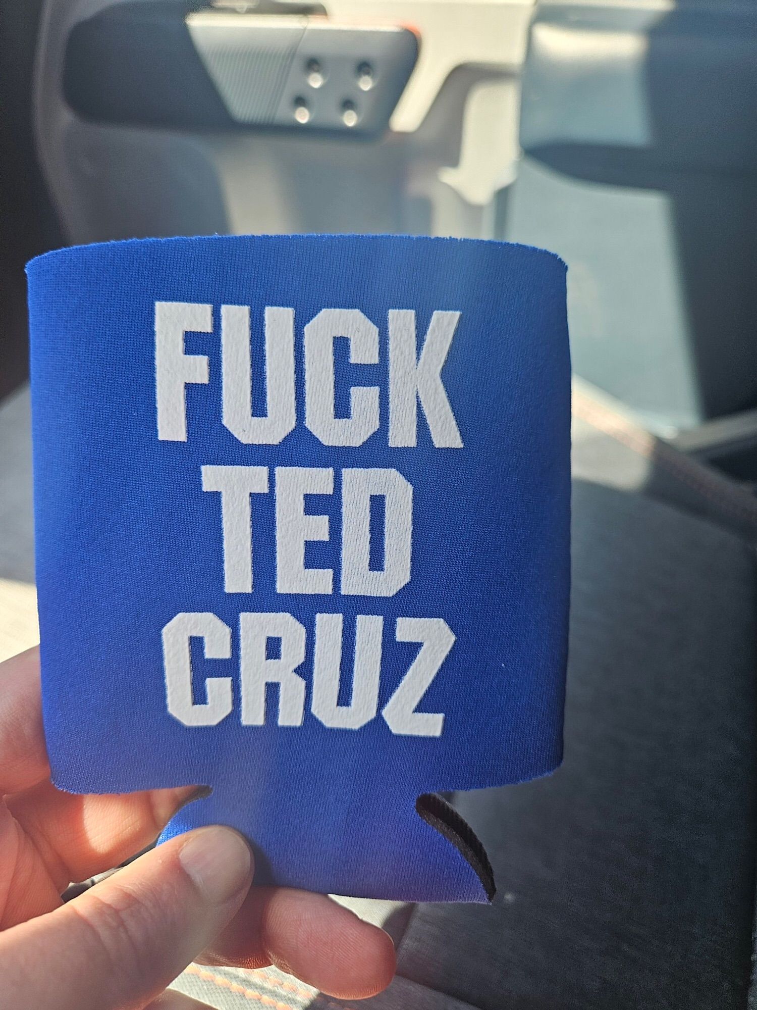 A white hand holds a blue and white koozie stating Fuck Ted Cruz.