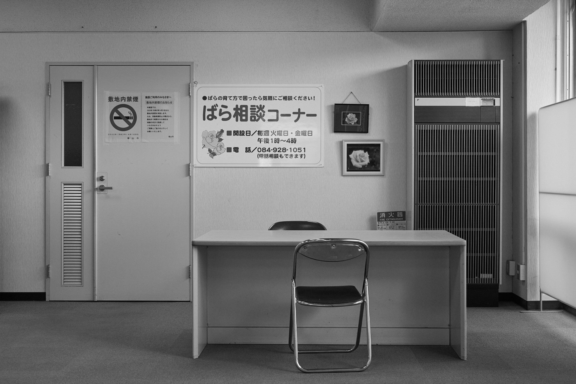 Black and white photo of a small office environment with a desk and two chairs.