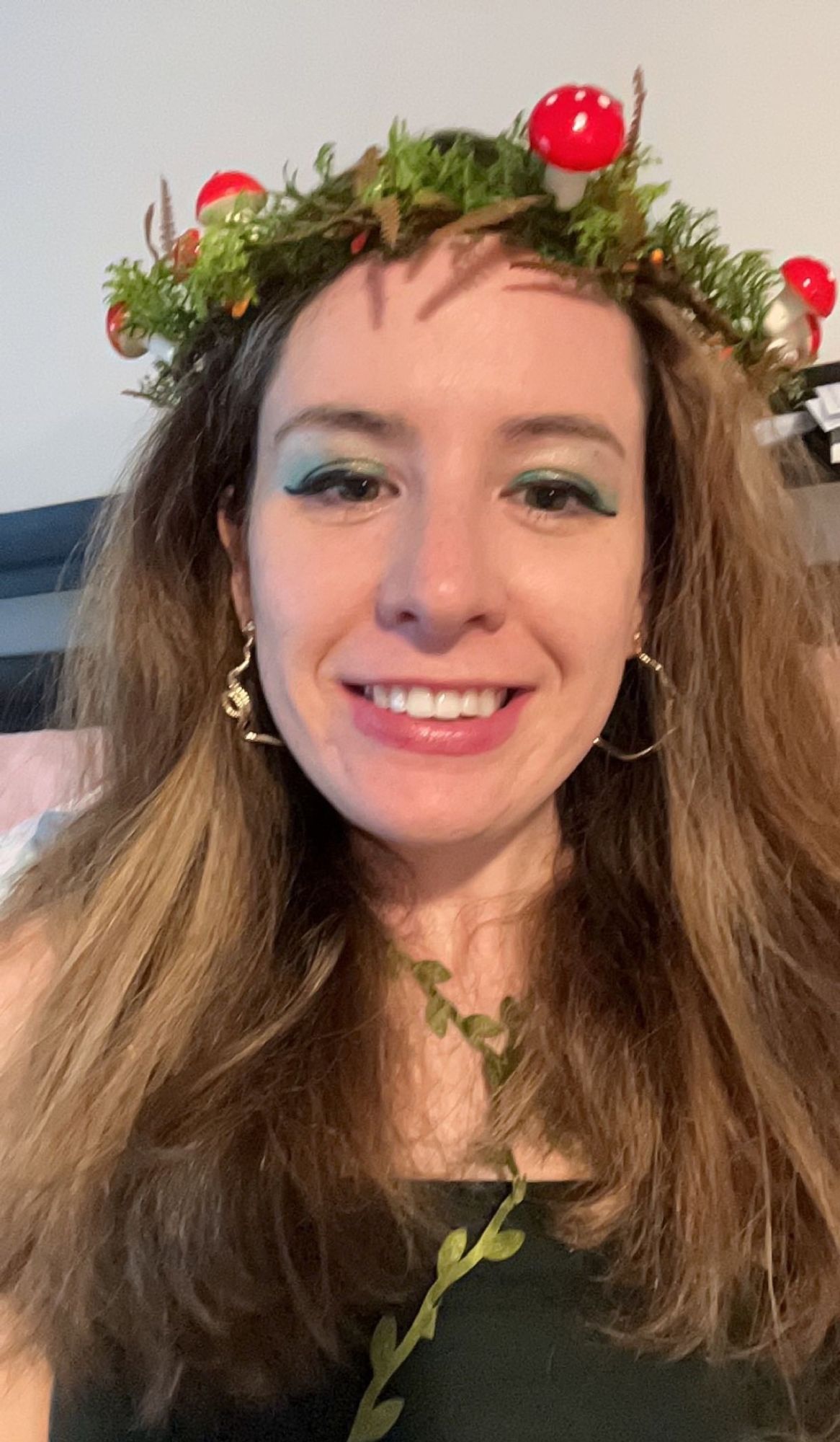 Im wearing a mushroom and fern flower crown, snake earrings, green eyeshadow, and a green tank with artificial vines tied over it