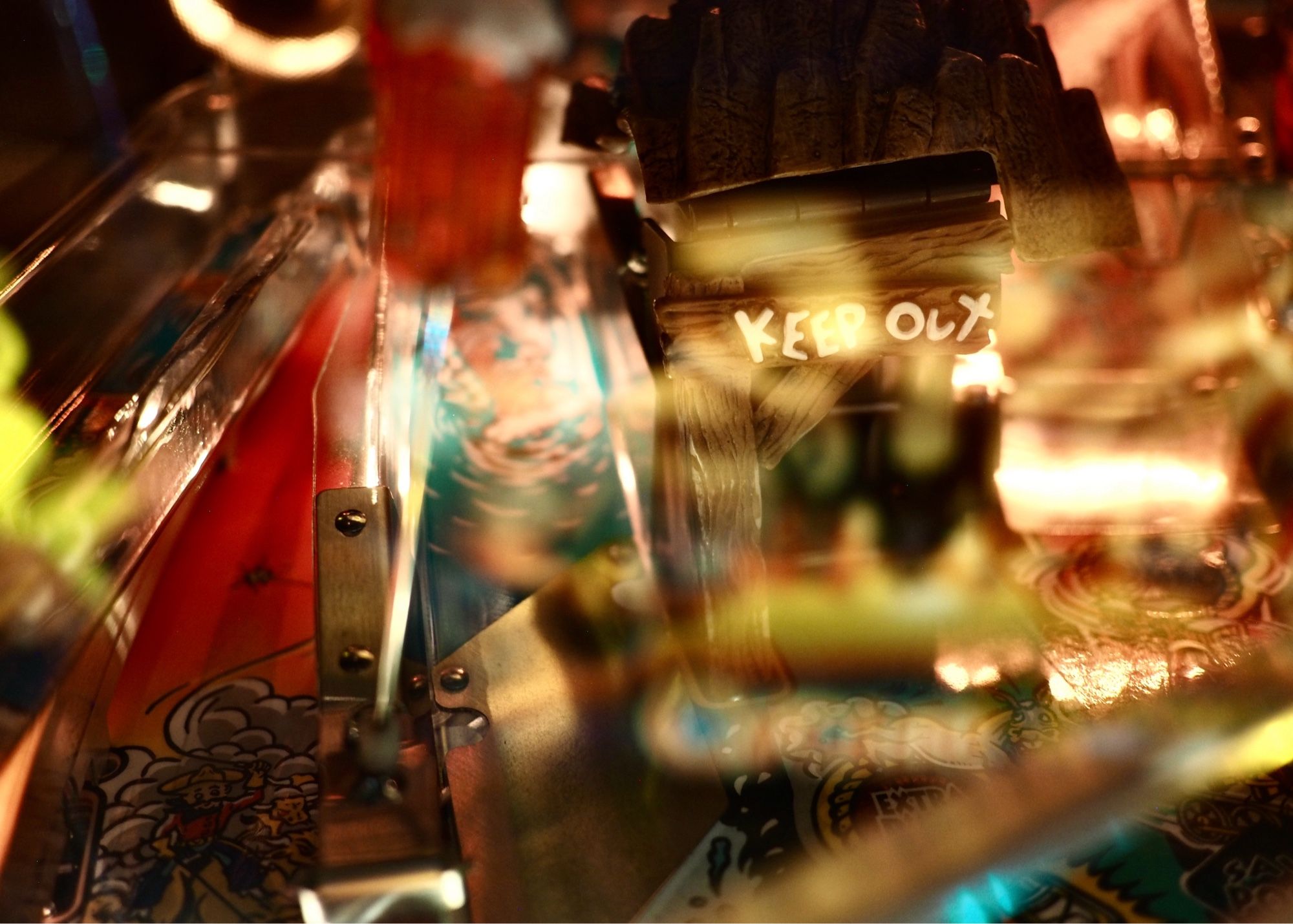 I forget what this pinball machine is, but it says KEEP OUT underneath a slurry of reflections off the glass of the table.