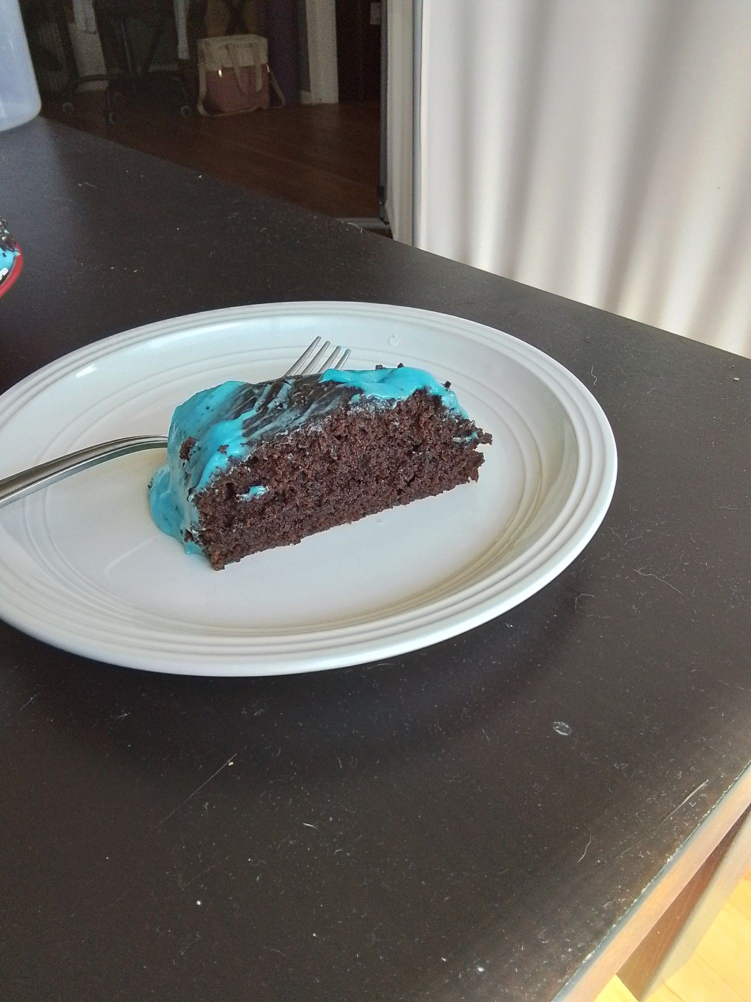 A lone slice of chocolate pumpkin cake with blue cream cheese icing. It's small and sits on a white plate.