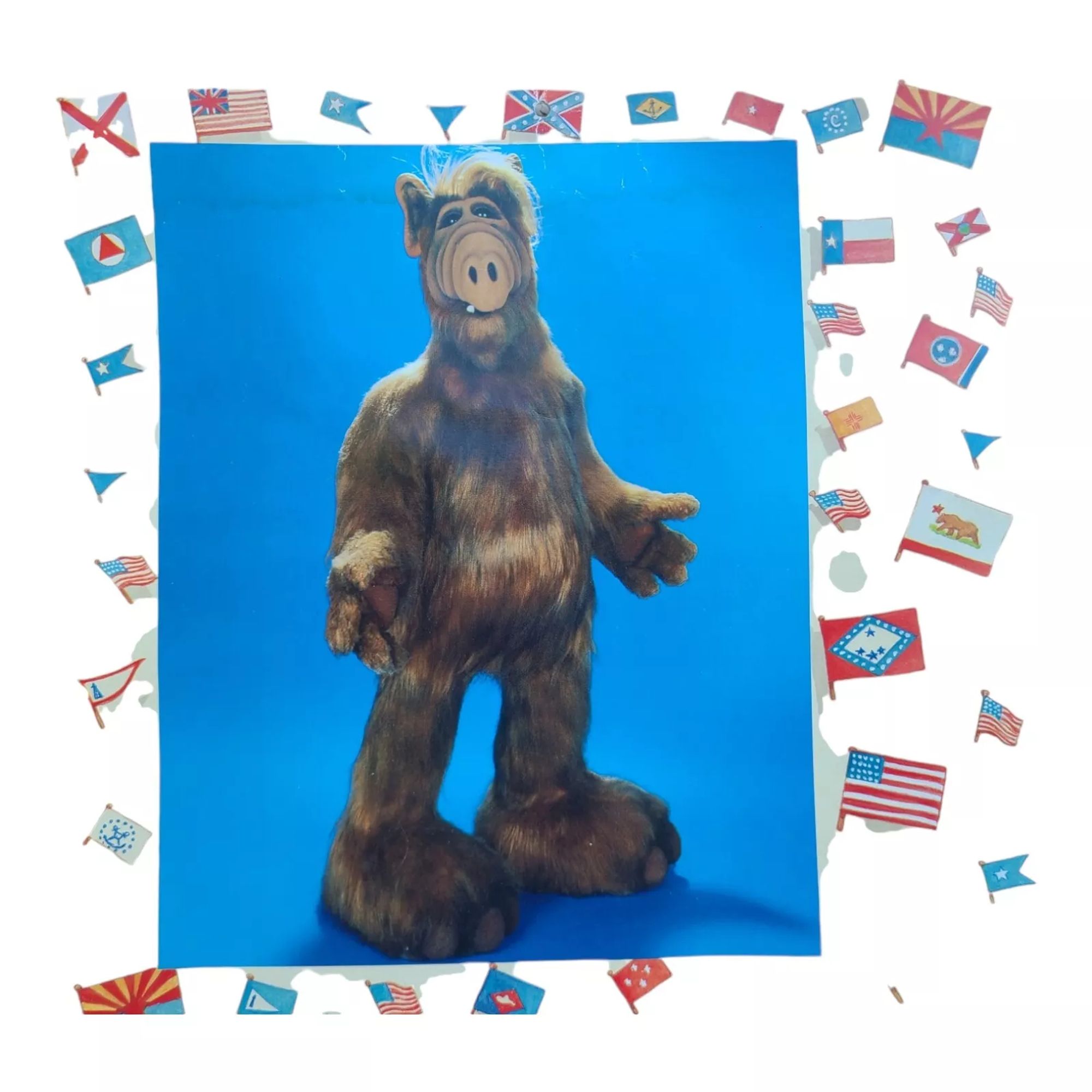 Page from the 1988 ALF calendar - July (Barp in the Melmacian calendar). Gordon stands against a blue backdrop, naked but for his luxurious fur. The page is adorned with US and state flags.