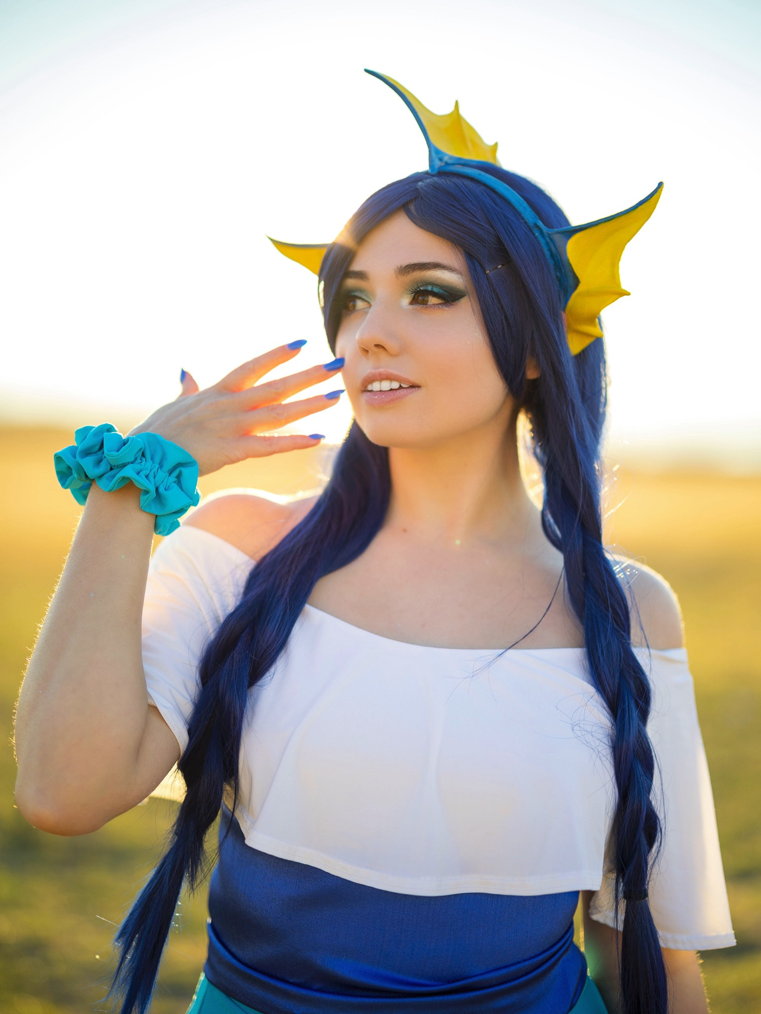 Charlee cosplaying as Vaporeon with a headband of yellow fins, long dark blue braids, a white off-shoulder top and dark blue bow around her waist