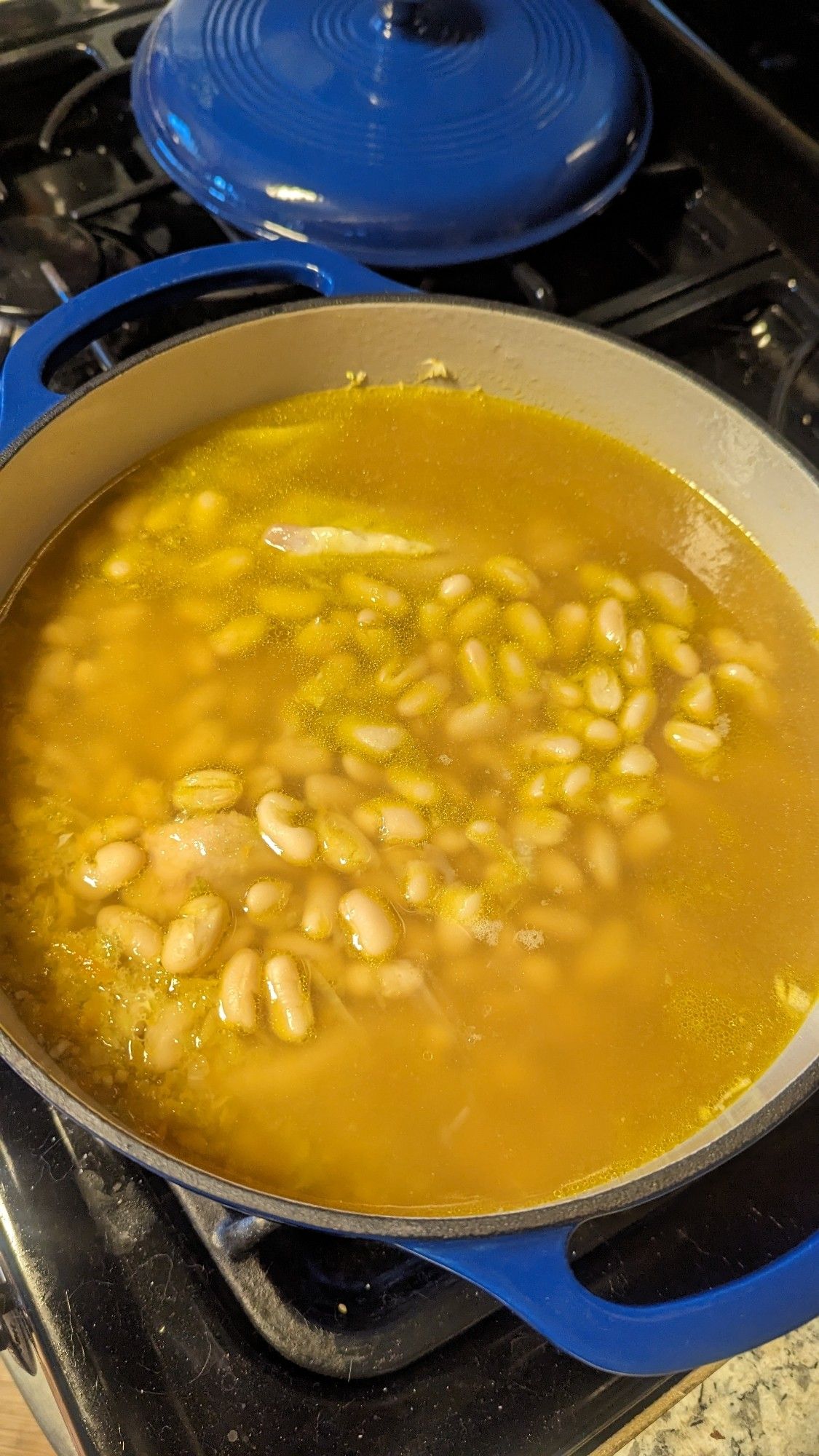 A pot of chicken cannellini soup in the making, with big white cannellini beans floating in chicken bone stock in a big cast iron pot, slowly coming to a boil