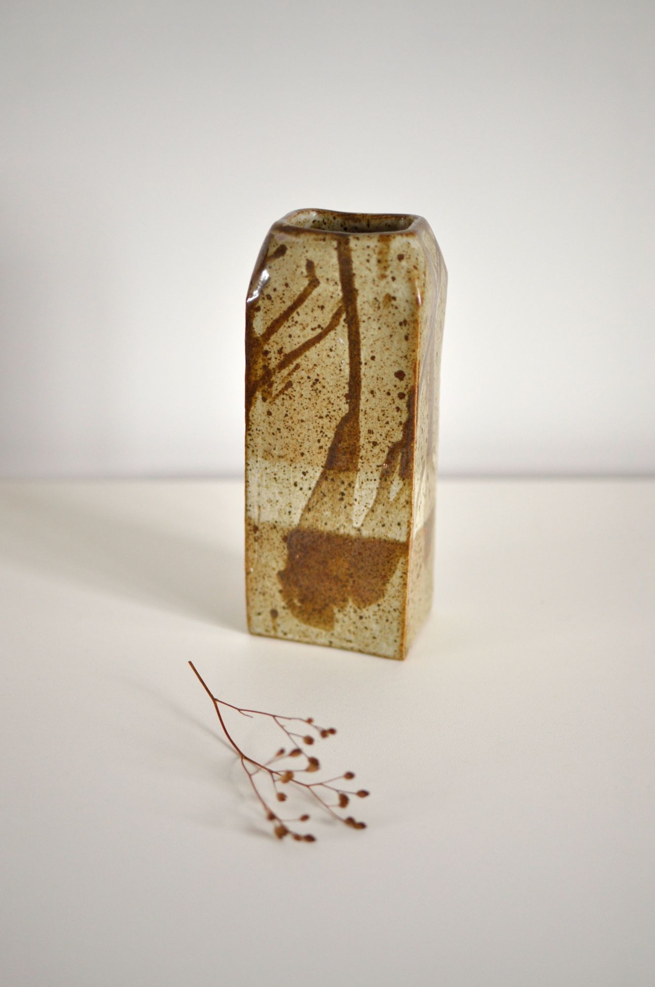 A vintage studio pottery vase handmade in a rectangular slab shape, in tones of beige and brown with an abstract drip glazed pattern.