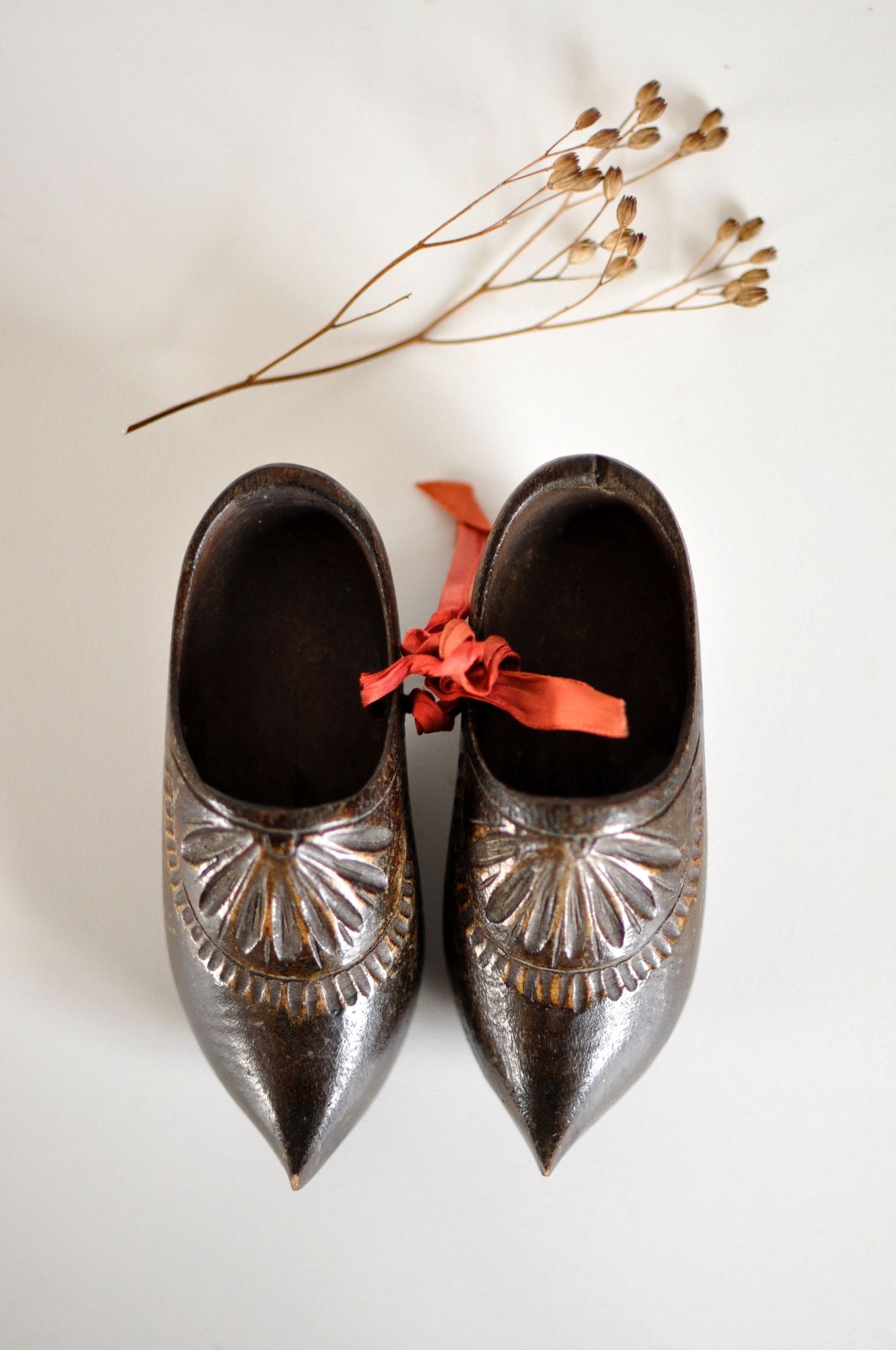 A pair of dark wood carved Dutch clogs tied with pink ribbon against a white background