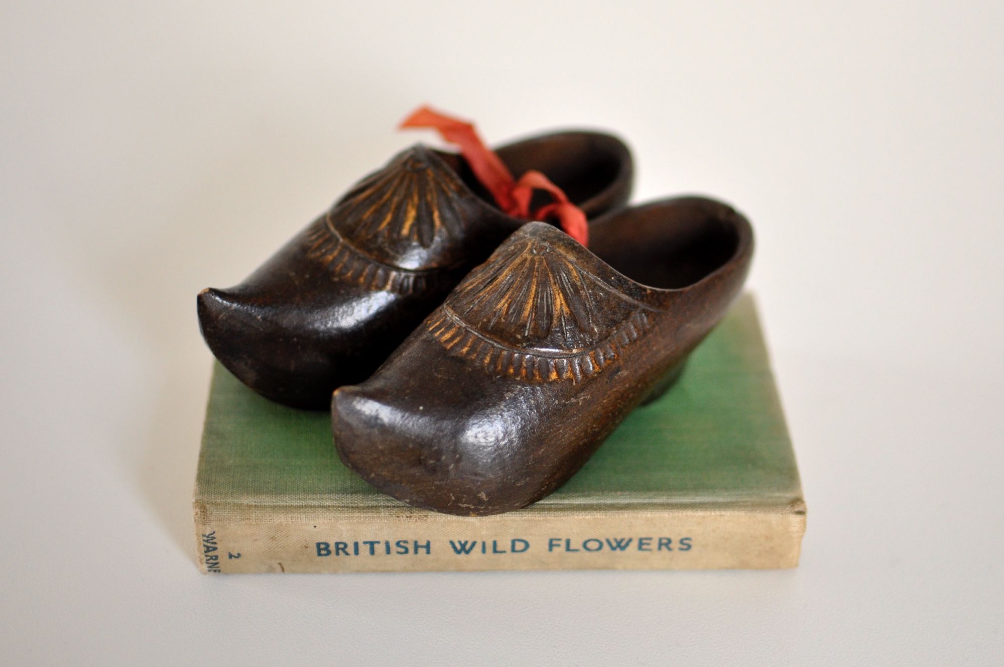 A pair of dark wooden mini Dutch clogs displayed on an old vintage green book they are tied together with old pink ribbon