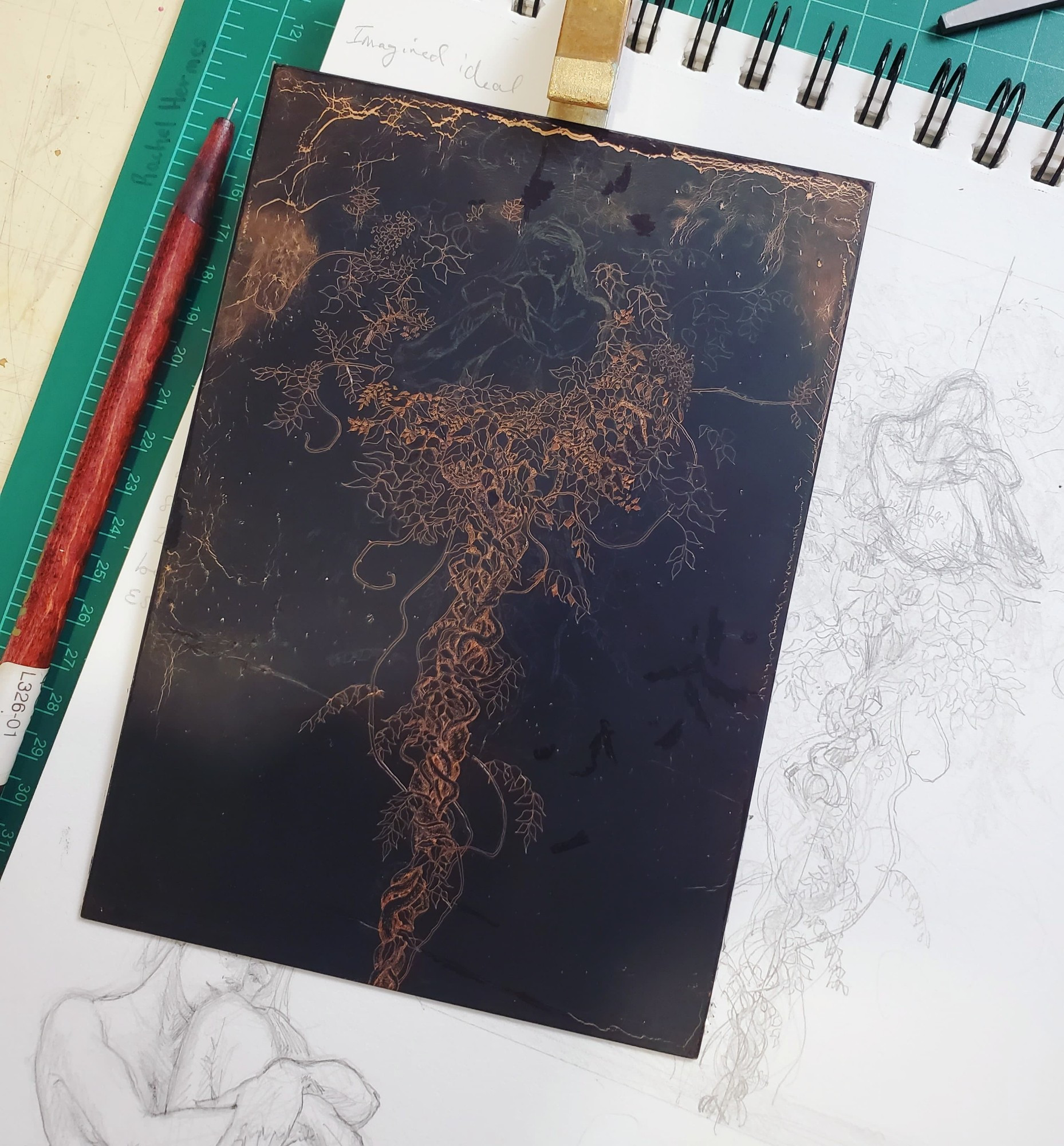 Photo of the copper plate etching (in progress) on top of a sketchbook page showing preparatory sketches for the piece. The plate is 5 by 7 inches.