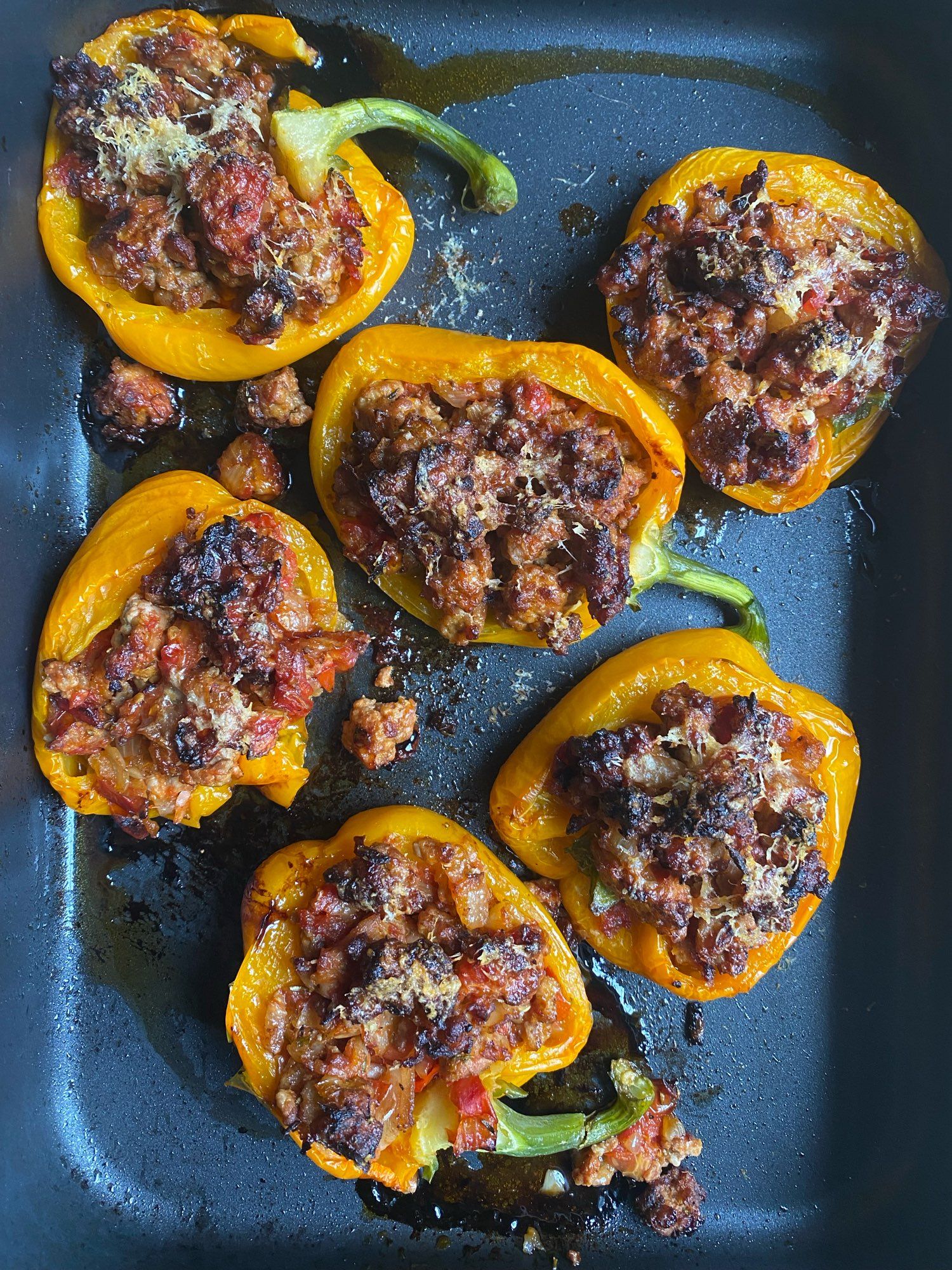 A black roasting tin filled with halved yellow peppers that have been stuffed with pork, herbs and Parmesan and baked.