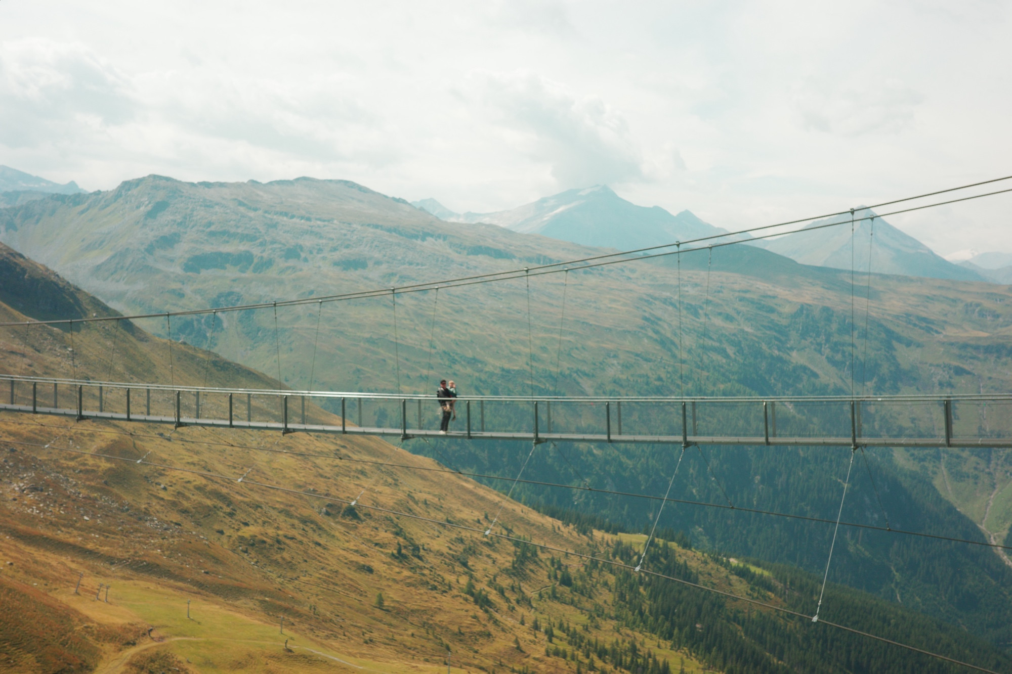 Mein Sohn und ich, sehr weit entfernt, auf einer Hängebrücke vor Bergpanorama. 