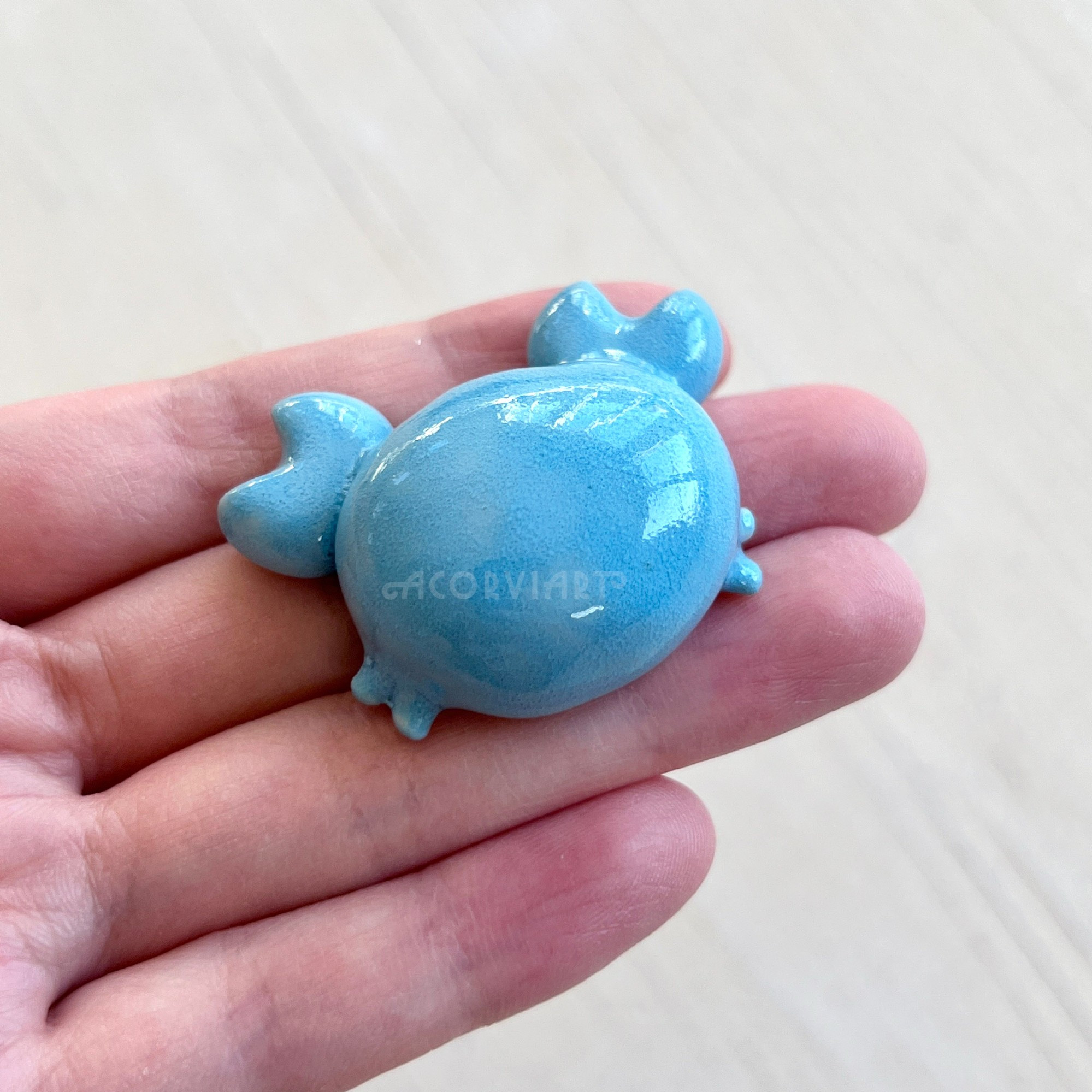 photo of a hand holding a small ceramic blue crab
