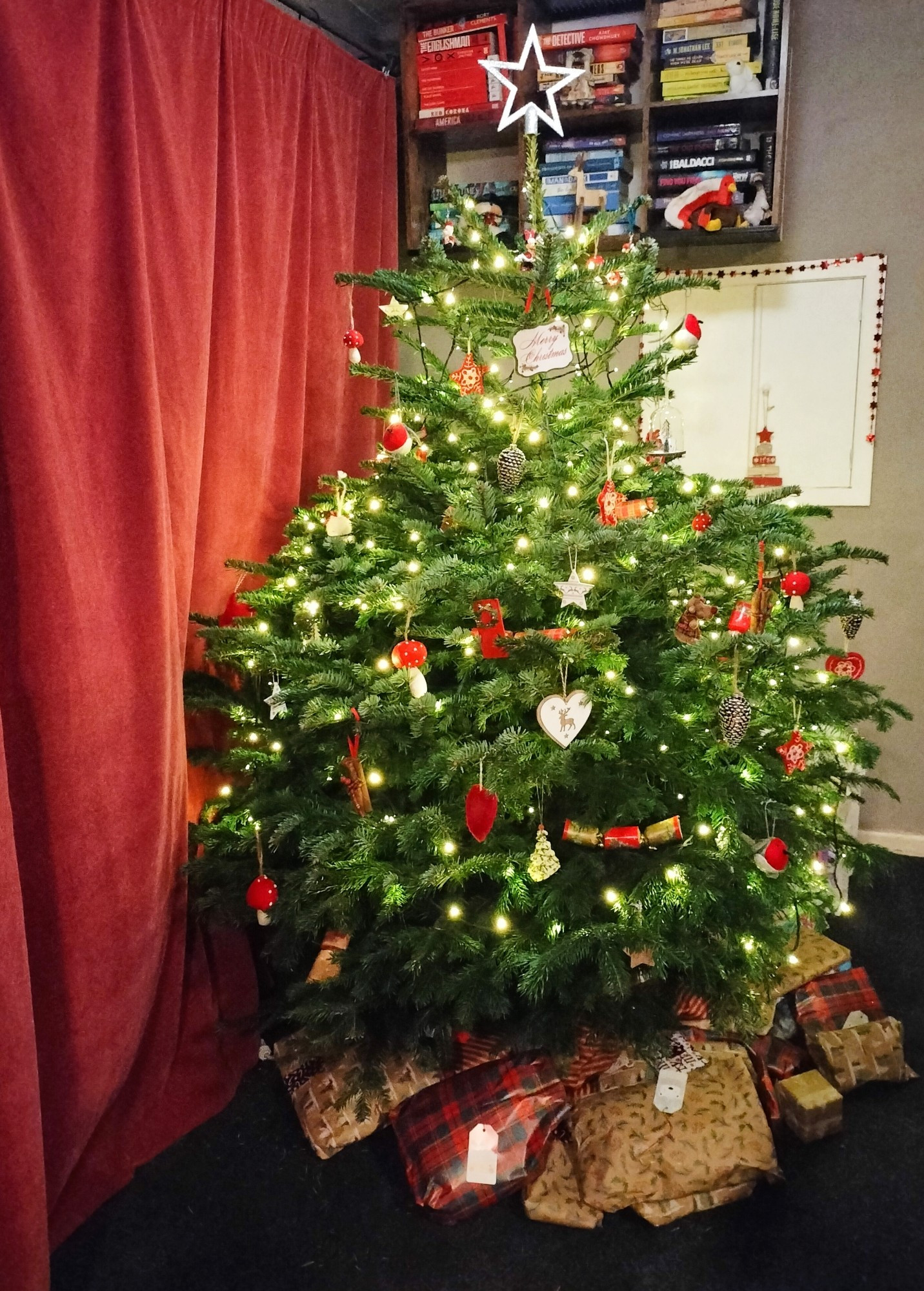 Photograph of a Christmas tree decorated with red and white decorations with a pile of presents underneath it.