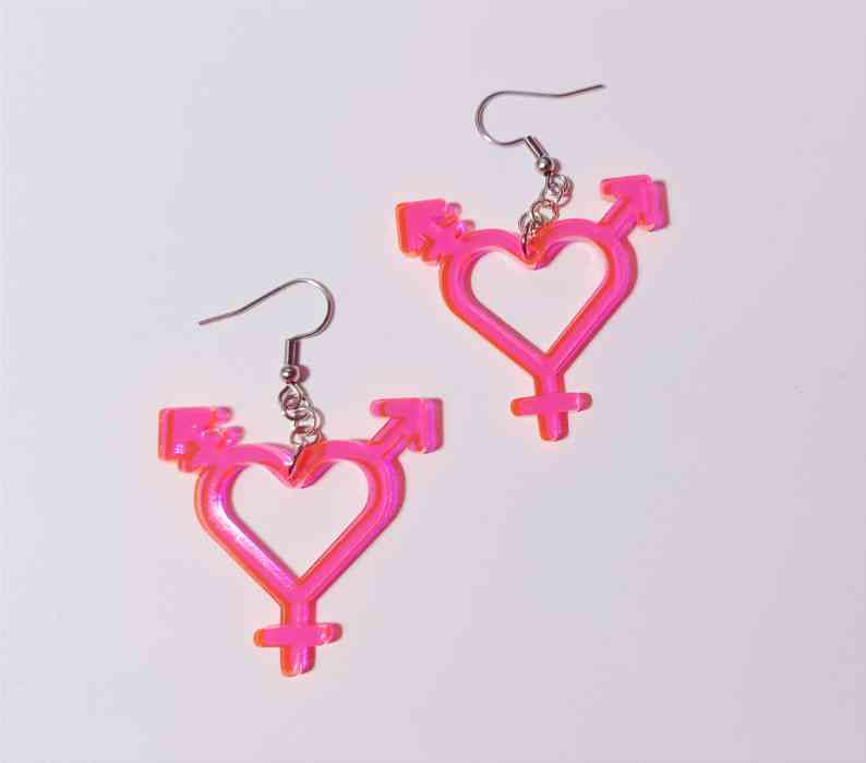 A pair of dangle earrings with vibrant pink acrylic charms in the shape of the transgender symbol, except the circle is replaced with a heart.
