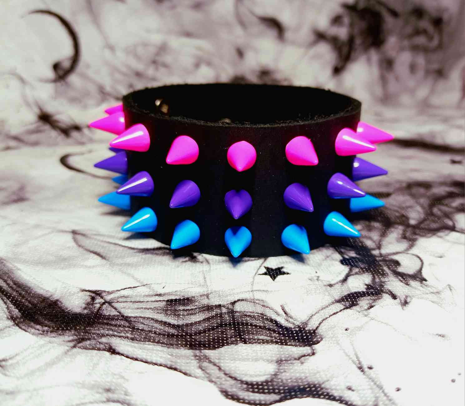 A leather wristband with short spikes arranged in the order of the 3-color bisexual pride flag
