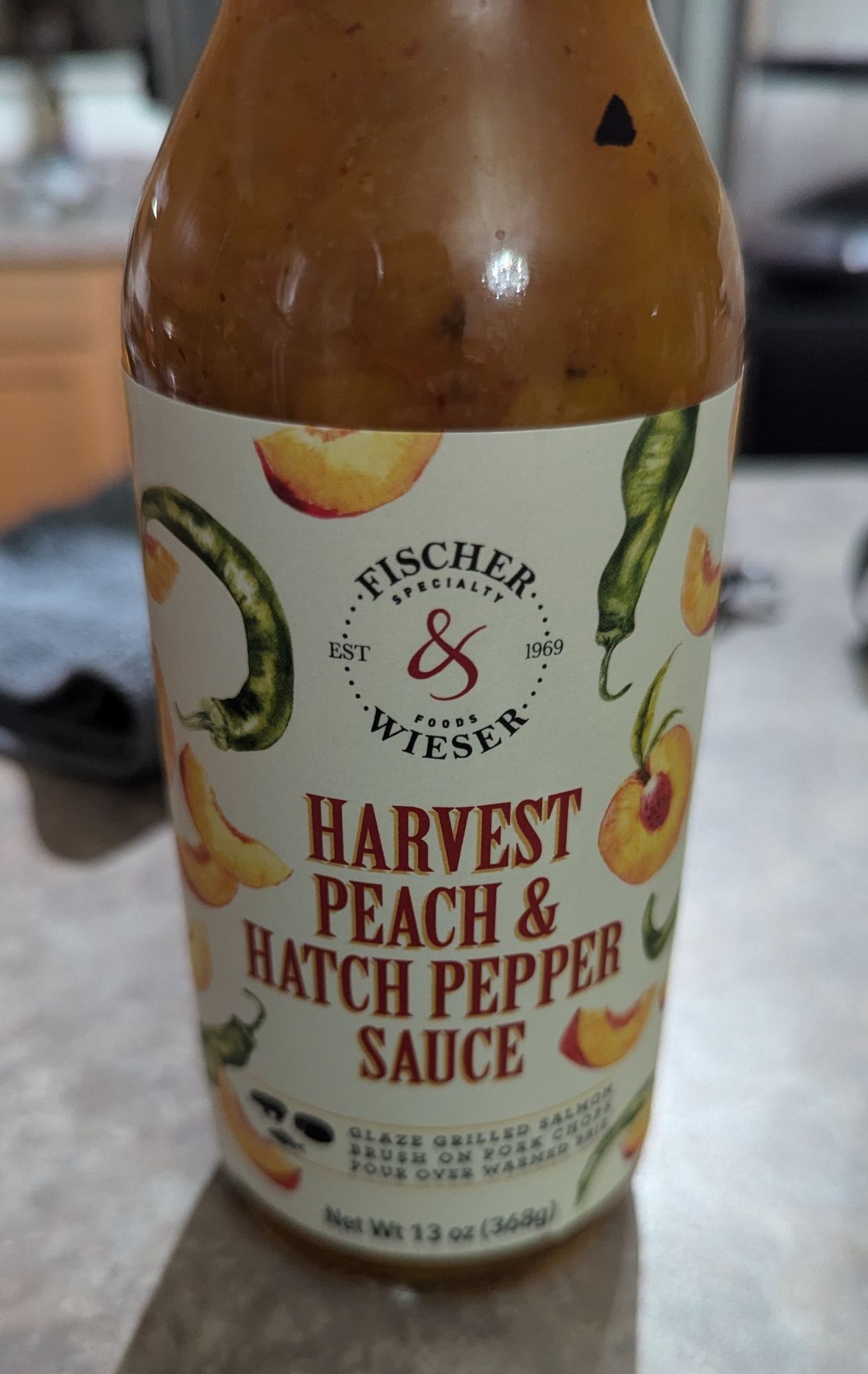 A jar or harvest peach and hatch pepper sauce on a counter.