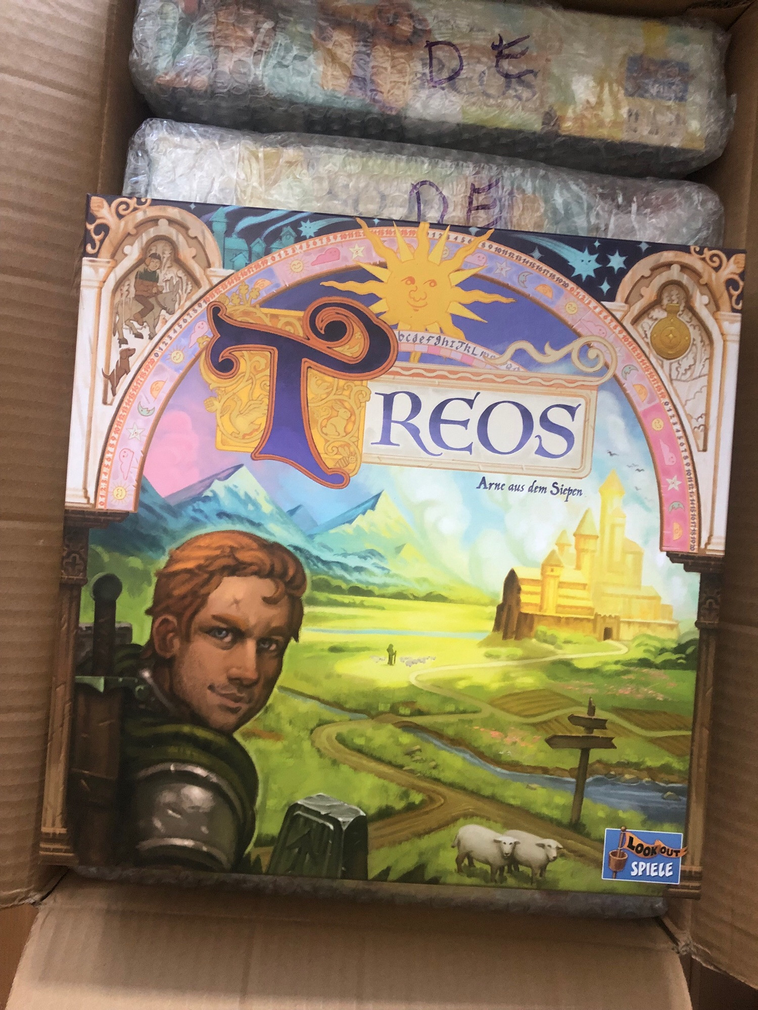 Cover box for TREOS boardgame, showing off one if the characters in medieval landscape; town in the background, sheep grazing in the front