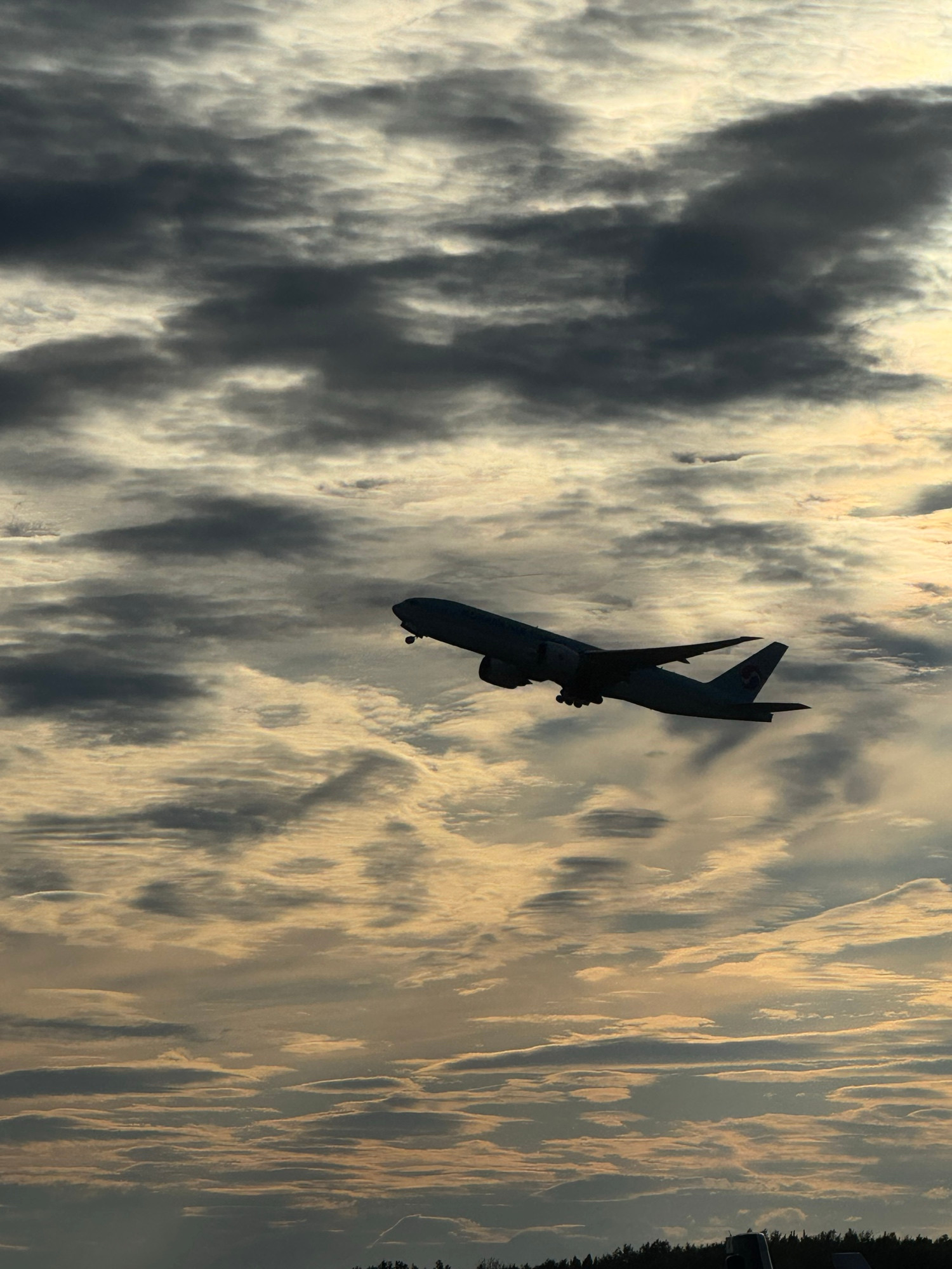 Silhouetted Korean Air Cargo 777-F against broken clouds in the evening sky taking off from Runway 15 at ANC. The gear is just starting to go up.