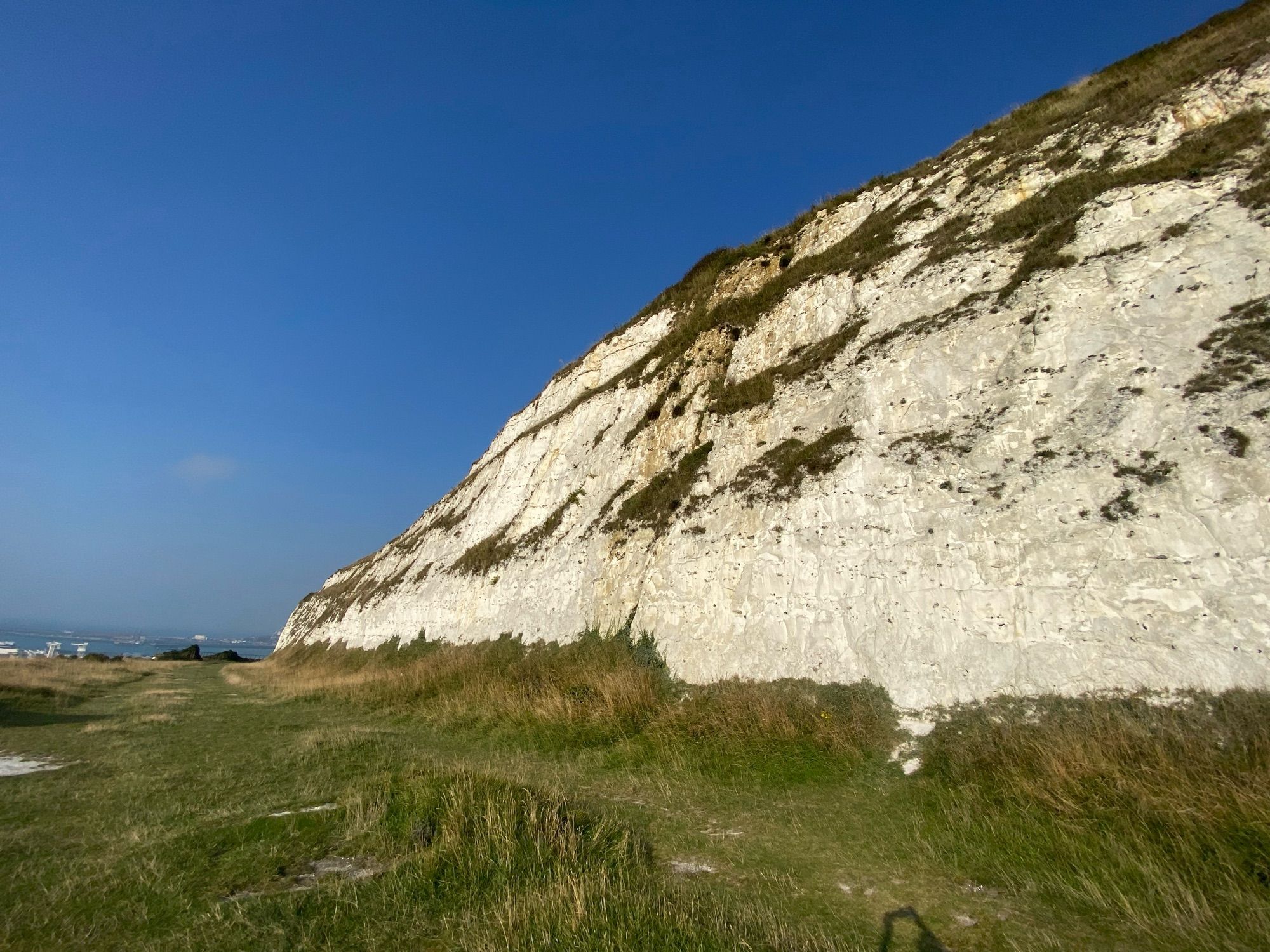 A white cliff composed of chalk. It is about 20 m tall. The sky is dazzlingly blue and cloudless