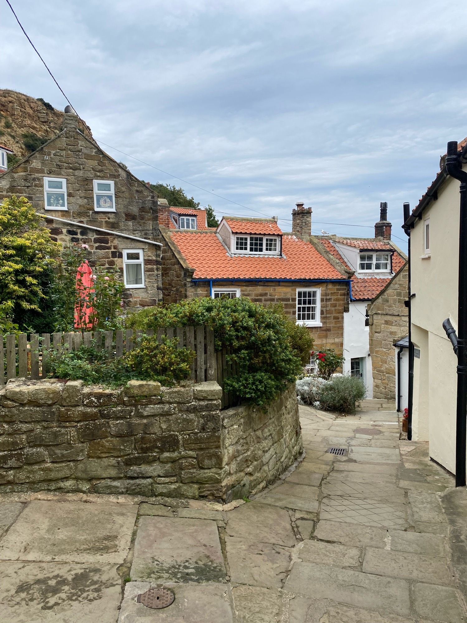 A view down a narrow passageway between light-brown very small, very pretty sandstone cottages. The sky is cloudy