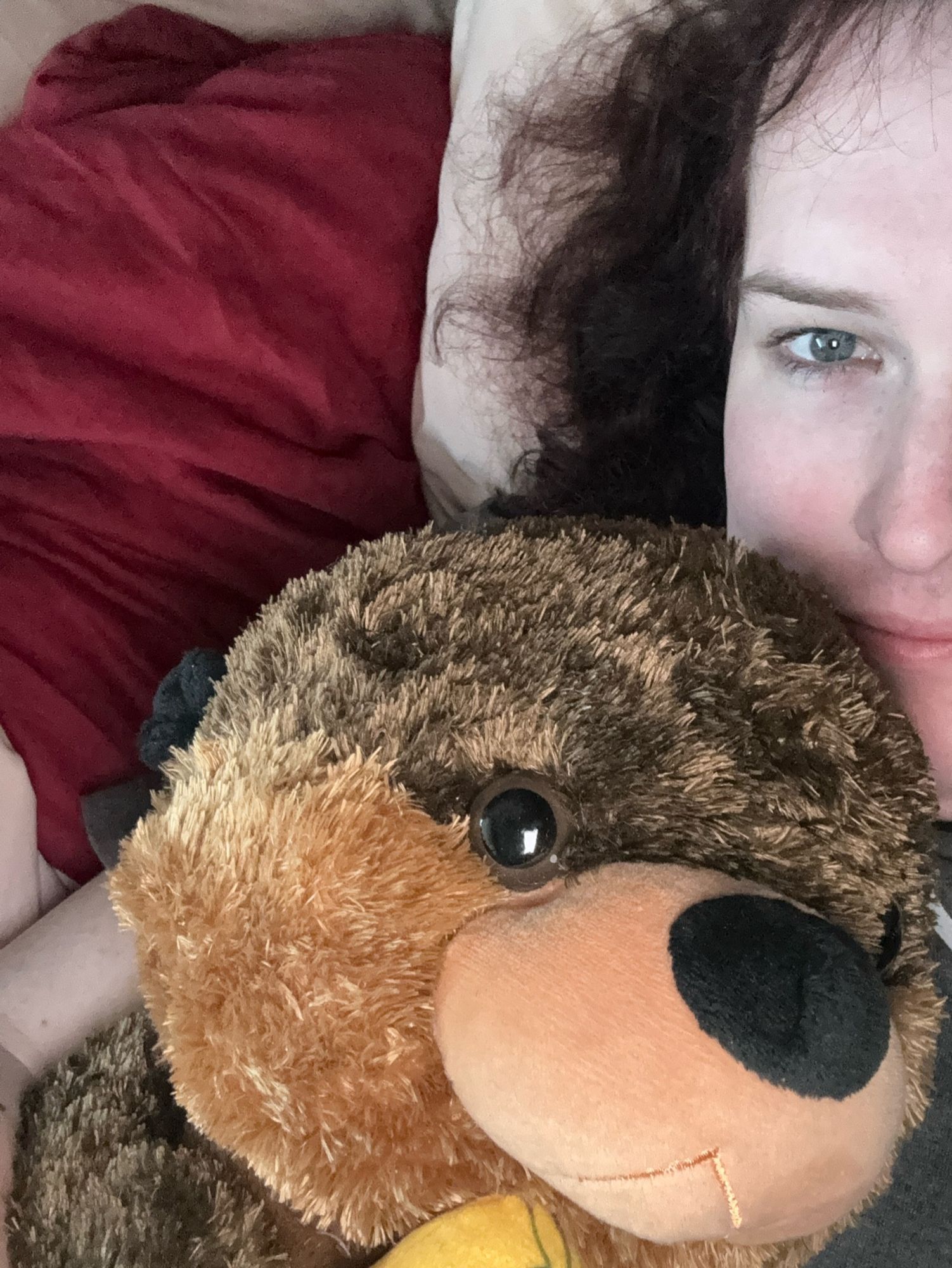 Mayja laying in her bed. Photo cropped to only show half of her face with the primary star of the pic being Squingus the stuffed otter