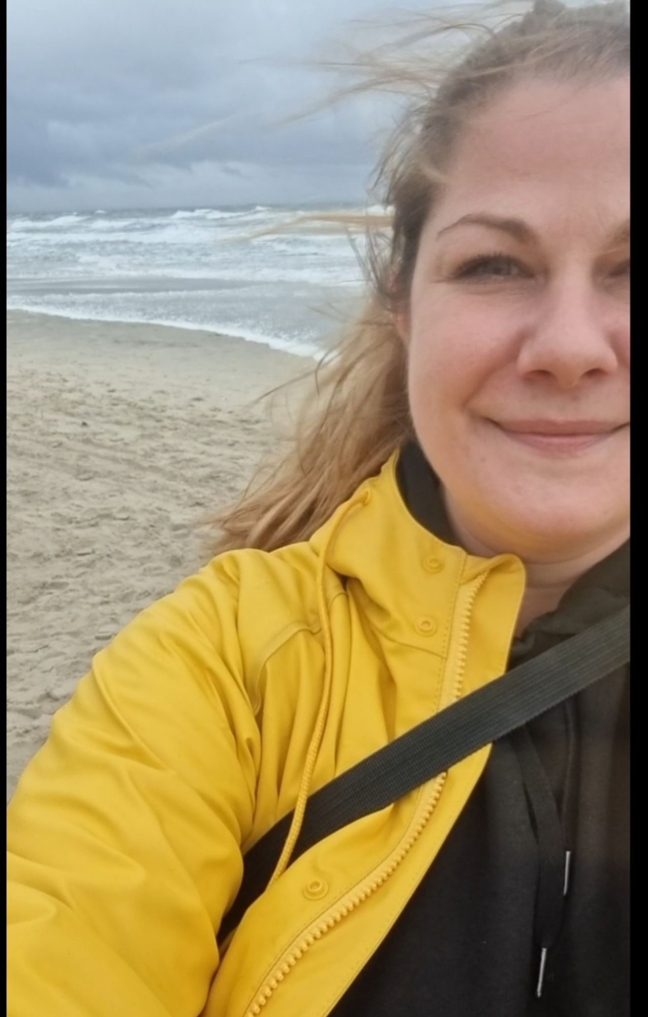 Selfie von mir im gelben Friesennerz. Im Hintergrund die Ostsee bei Sturm.