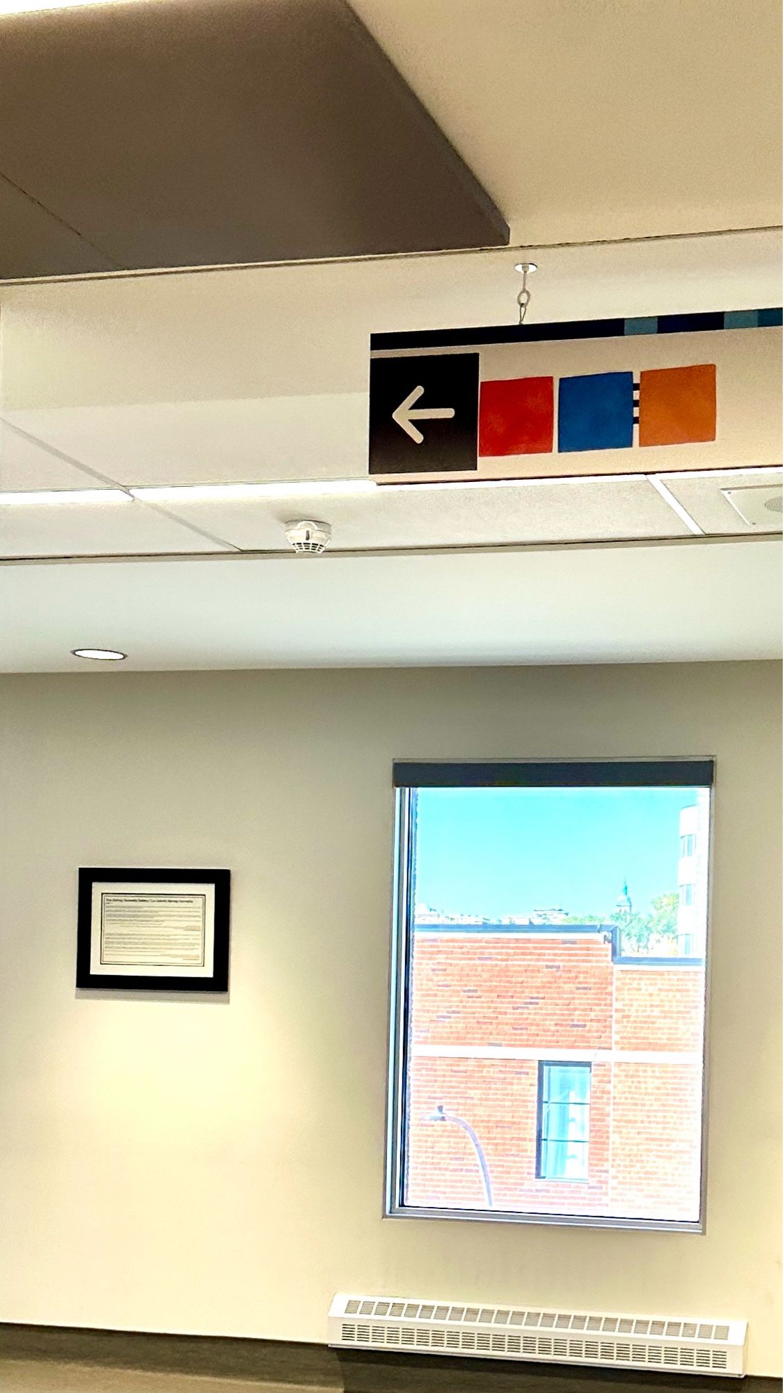 The image features a directional sign indicating "left" above colorful rectangular panels, with a framed document on the wall and a window showing brick buildings outside