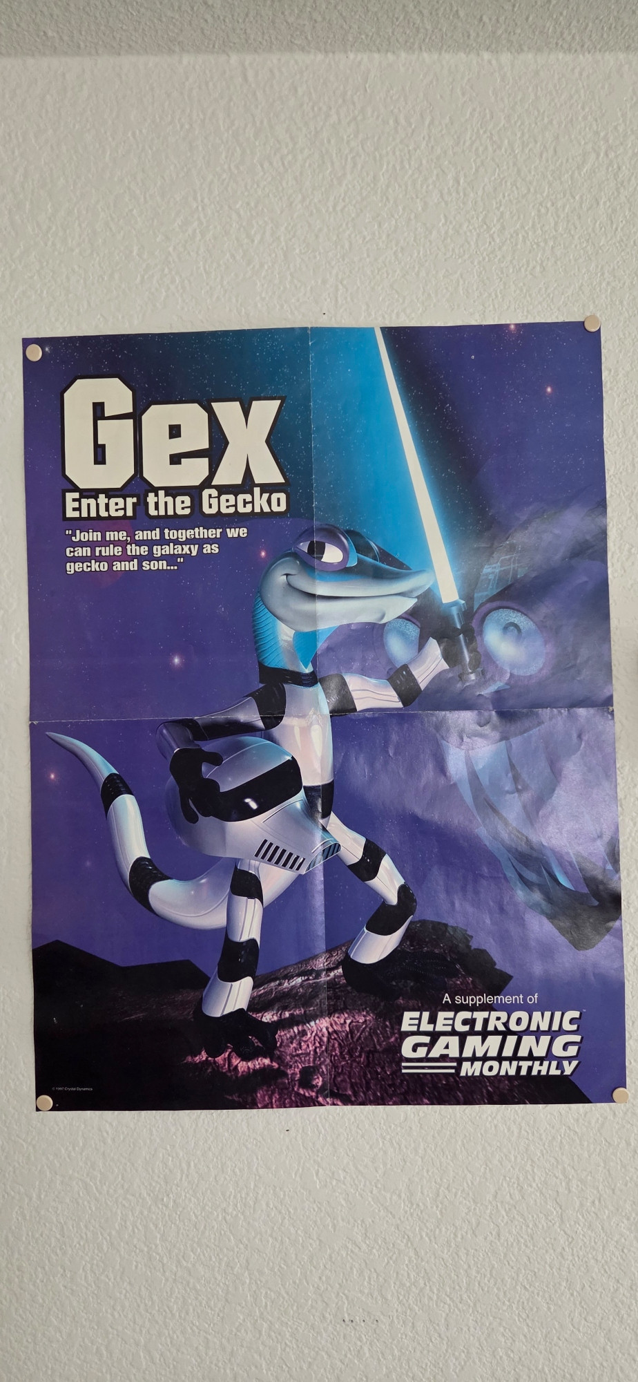 Poster of Gex the Gecko from Gex Enter the Gecko brandishing a green lightsaber while clad in a Star Wars stormtrooper uniform, helmet under his other arm.