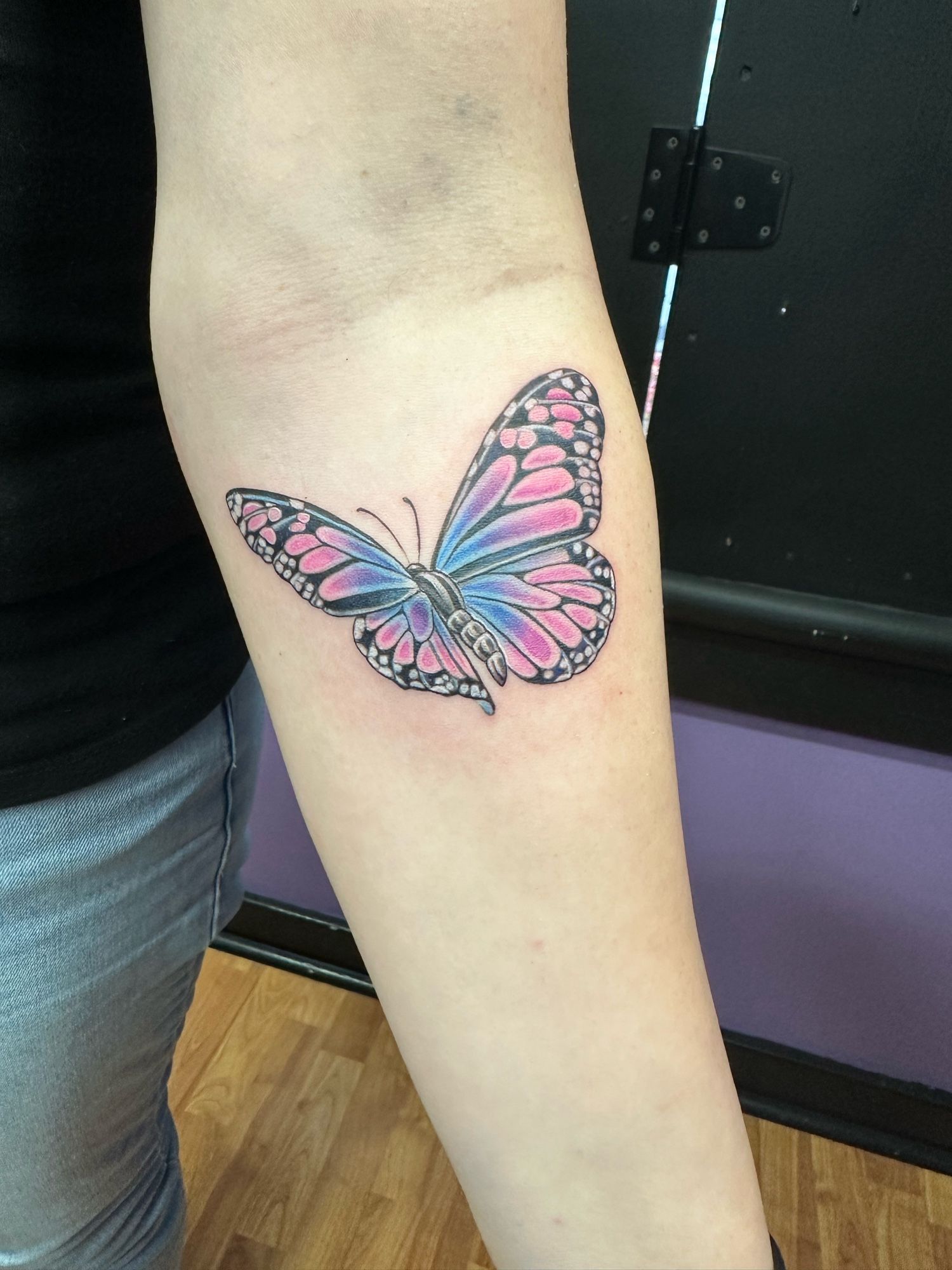 A blue and pink monarch butterfly on a woman’s forearm. It is very pretty.