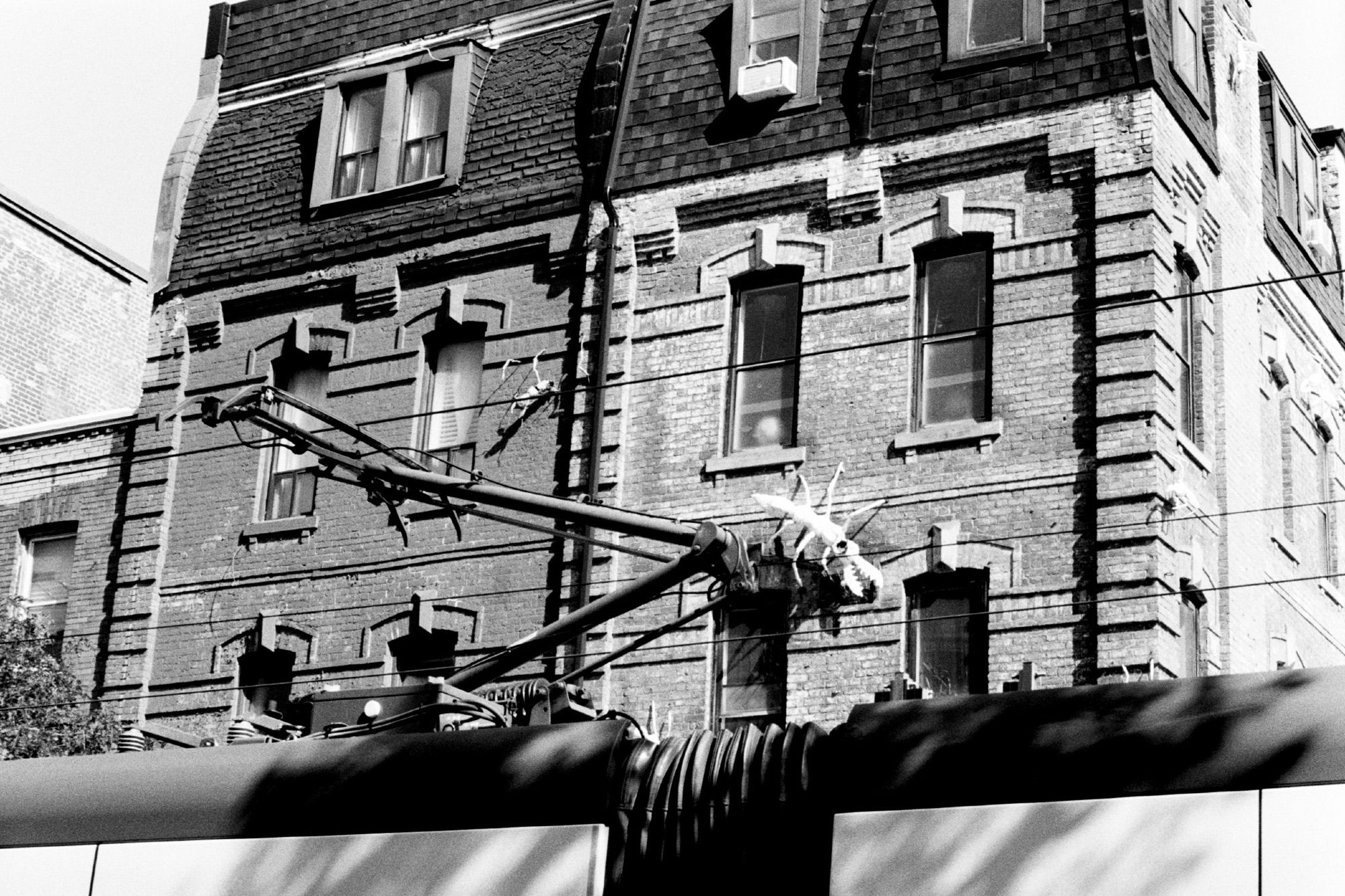 Low-angle view of a venue with distinctive ants mounted to the exterior. A street car passed while I was making the photo, so to the bottom of the frame is the top of the vehicle and its pantograph drawing power from the catenary overhead.