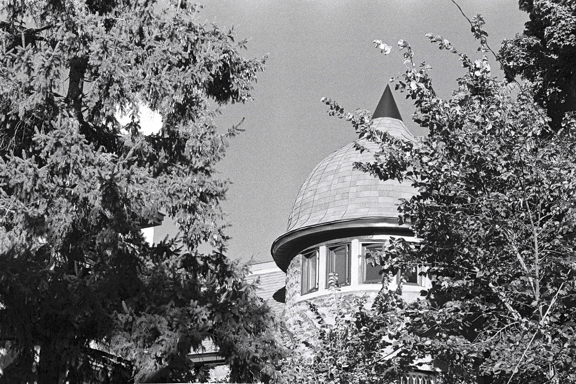 Upper floor of a home-converted-to-apartment with a cupola. Two of the windows are open, allowing early Fall breezes in. It is framed on either side with trees.