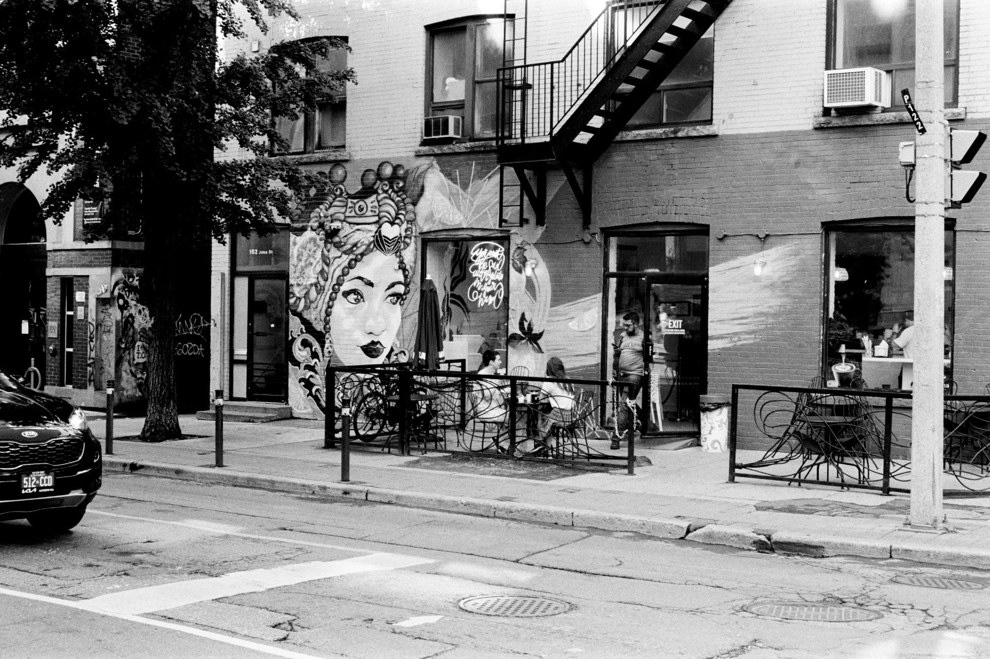 People enjoying morning coffee on a patio. A man from inside the coffee shop is seeking a table on the patio.