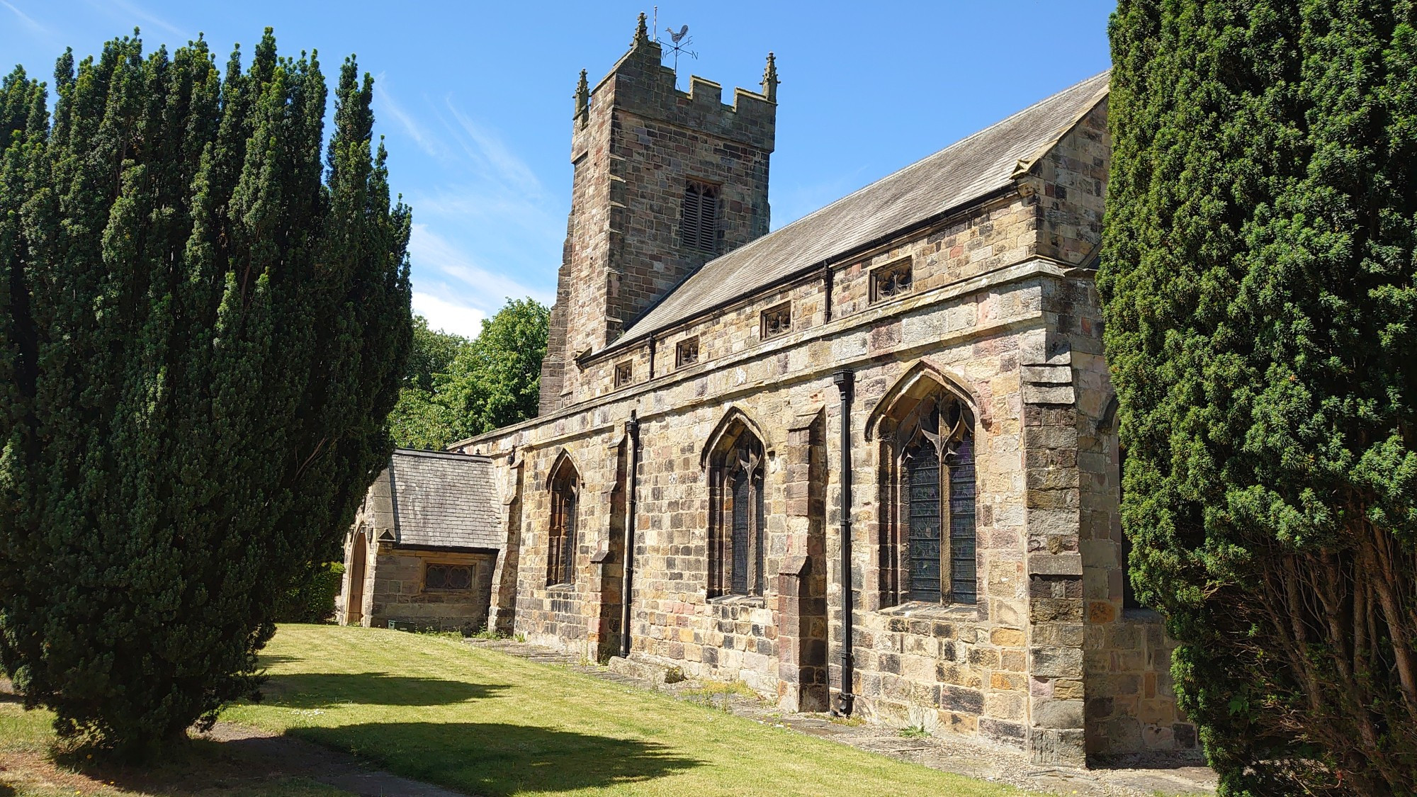 Photo of an old church with trees and grass in the foreground and blue sky above.