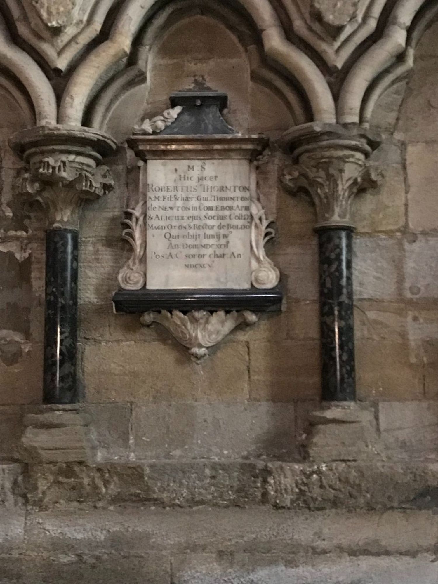 A stone memorial on the wall in Durham Cathedral, with decorative pillars.