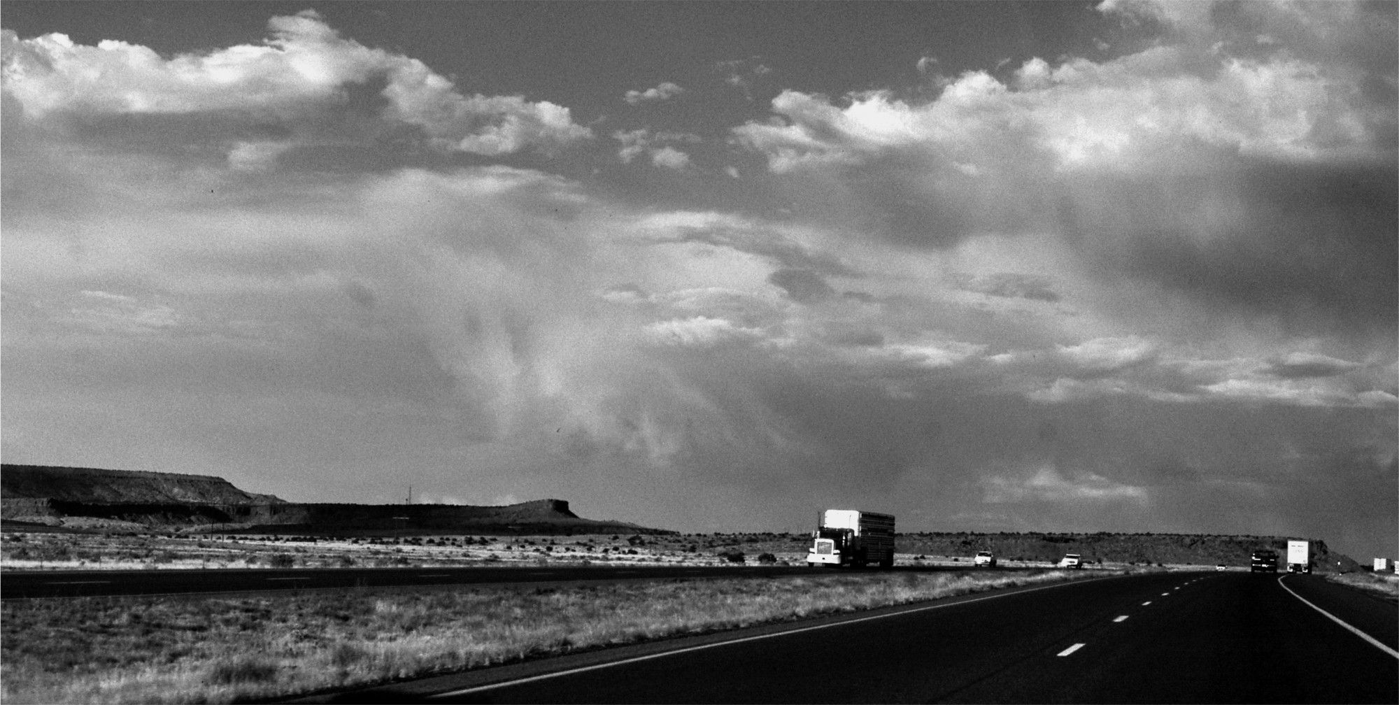 Schwarzweiß: auf einem US-Highway in steppenartiger Landschaft auf Straße mit ein paar Trucks unter dramatischem Wolkenhimmel