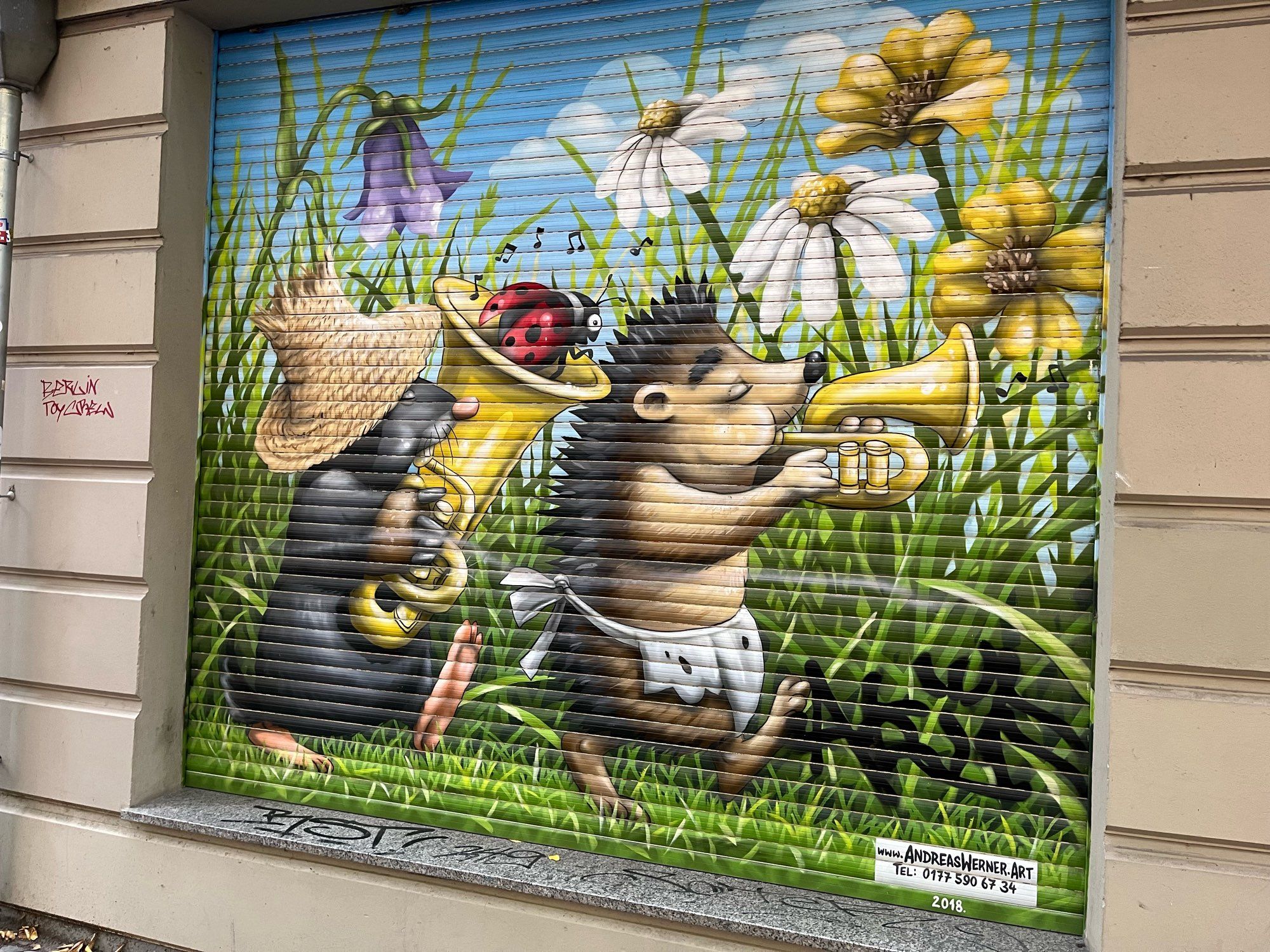 A mural painted on store shutters somewhere in Berlin. A shrew with a tuba and a hedgehog with a trumpet in a field of flowers.