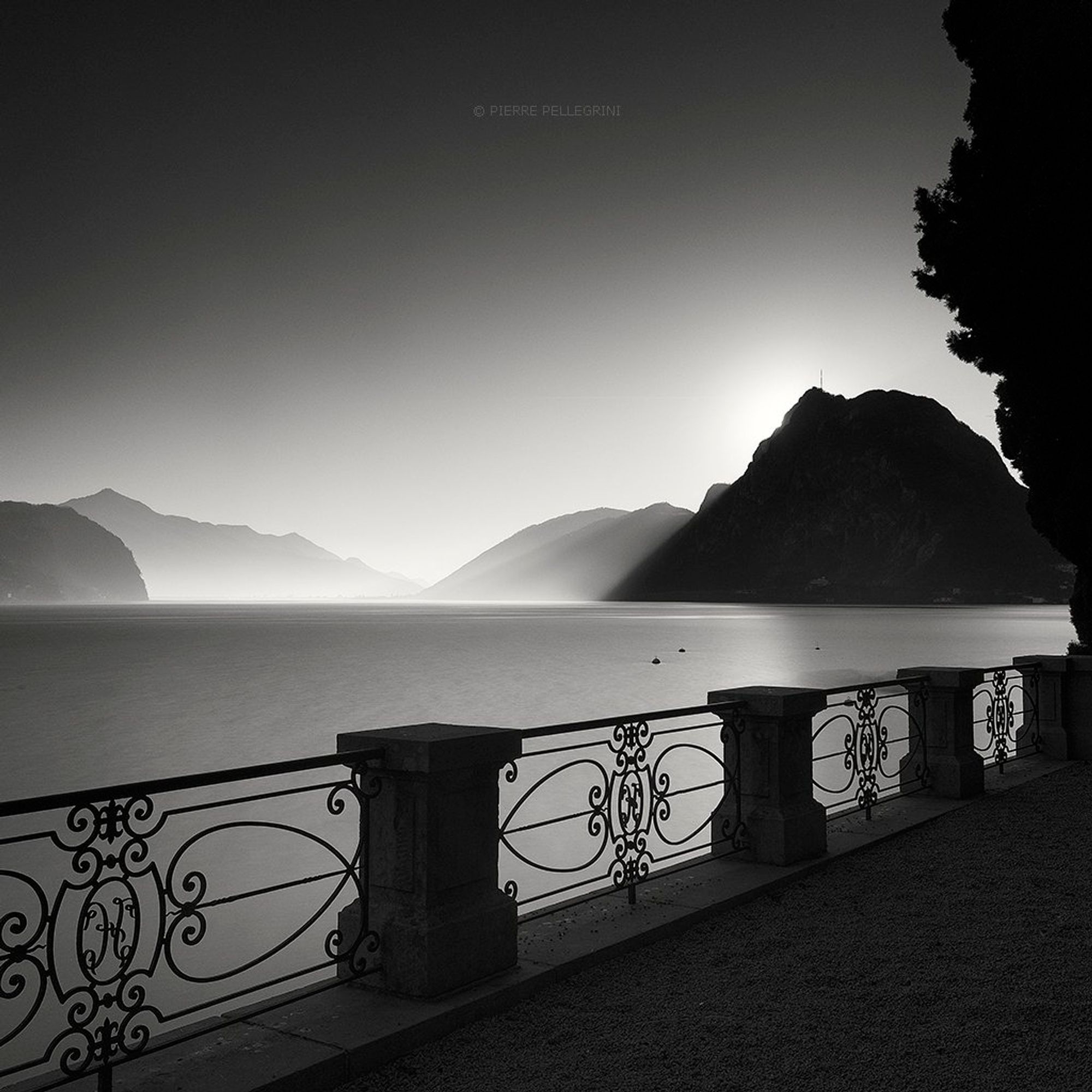 View of the lake from a terrace, with curved wrought iron fence and layered mountains in the background