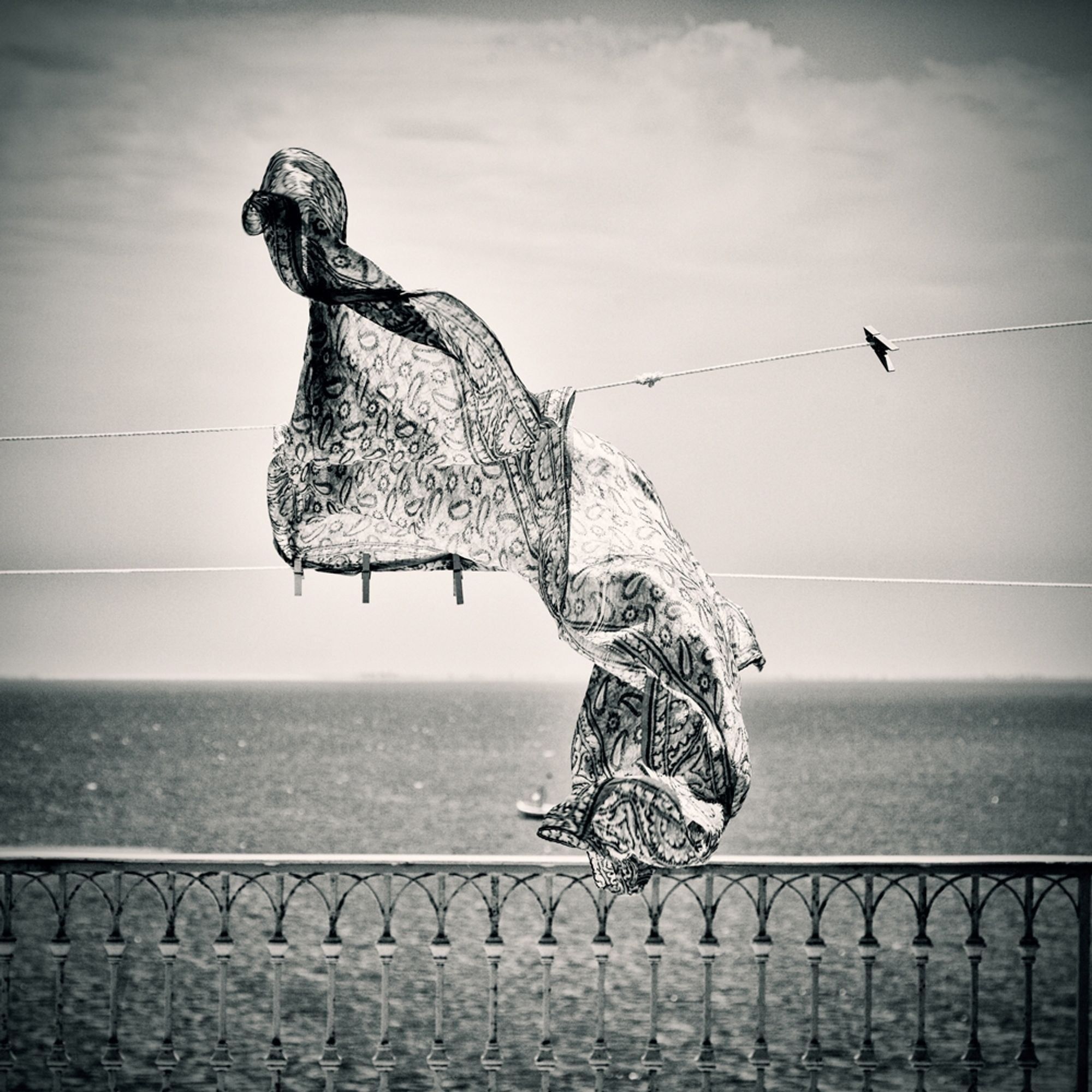 A breeze lifts a scarf pinned to closeline above a wrought iron terrace fence overlooking the Mediterranean