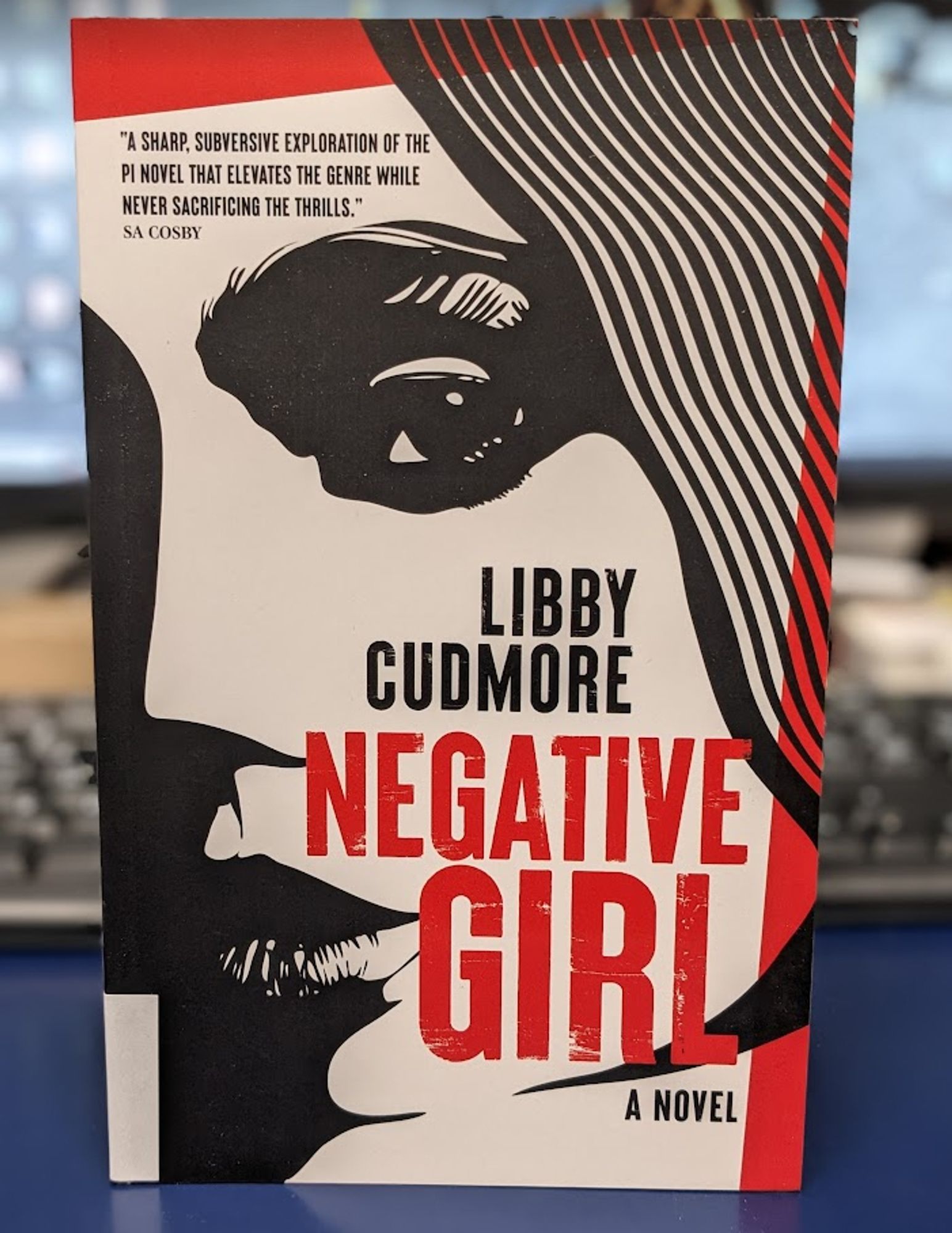 a paperback copy of Libby Cudmore's NEW NOVEL, Negative Girl, on my blue library desk