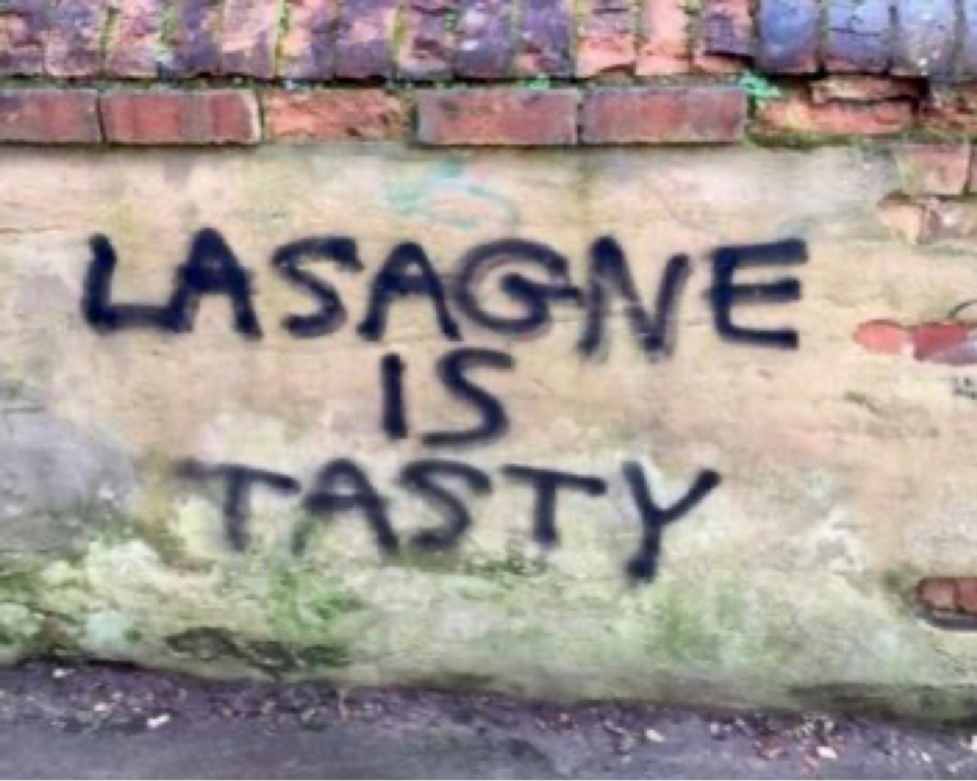 Graffiti in black spray paint on a wall reads “LASAGNA IS TASTY.”