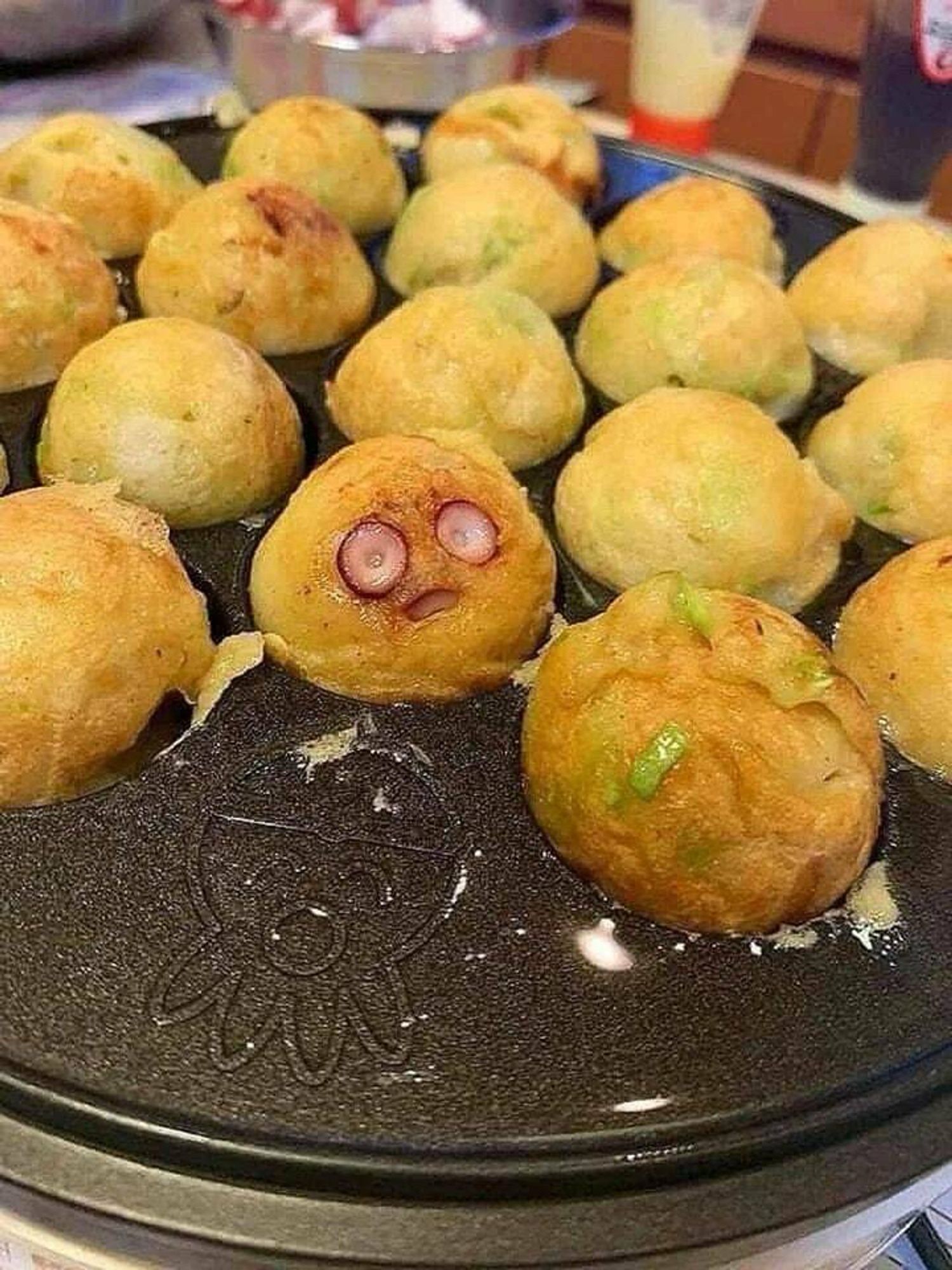 A round, fried hors d'oeuvre sits on a plate with a shocked expression. It is surrounded by others like it, except for an empty spot next to it.