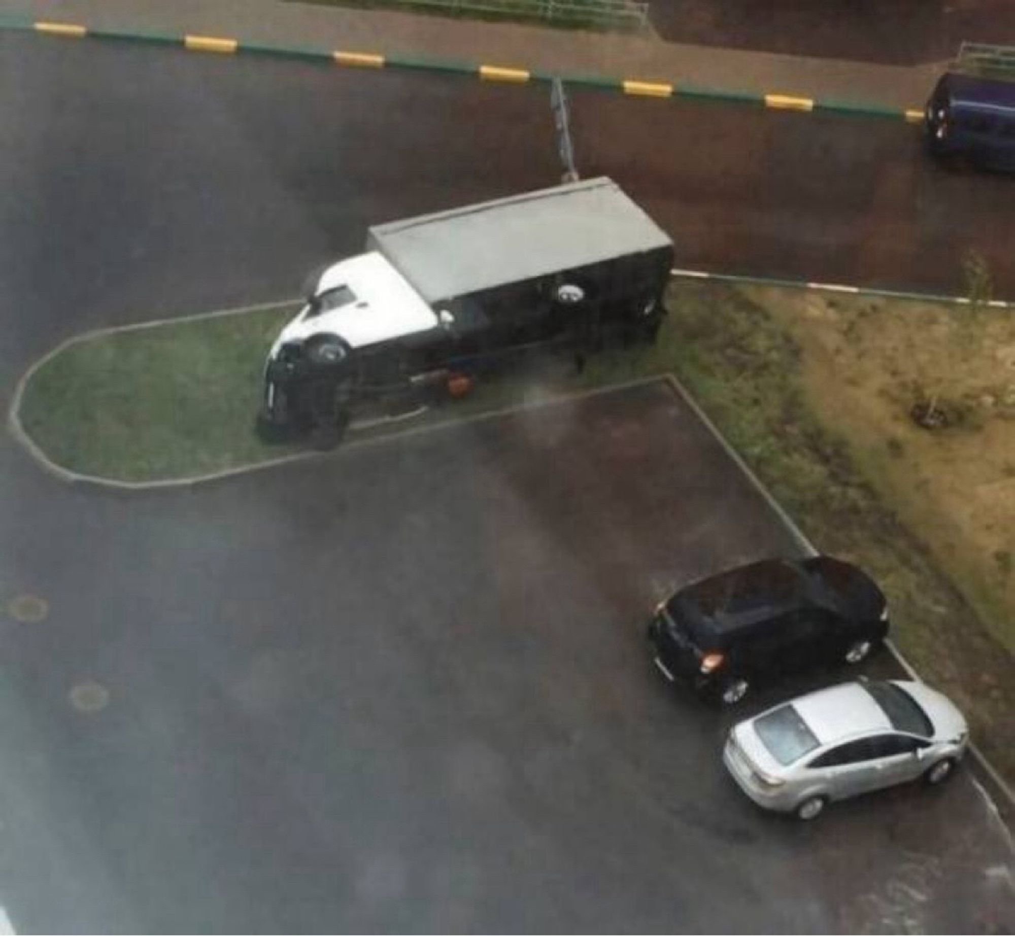 A truck lies on its side on a grassy spot adjacent to a parking lot.