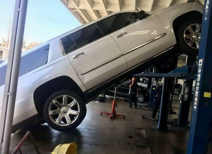 A white Cadillac Escalade hangs off a mechanic's lift.