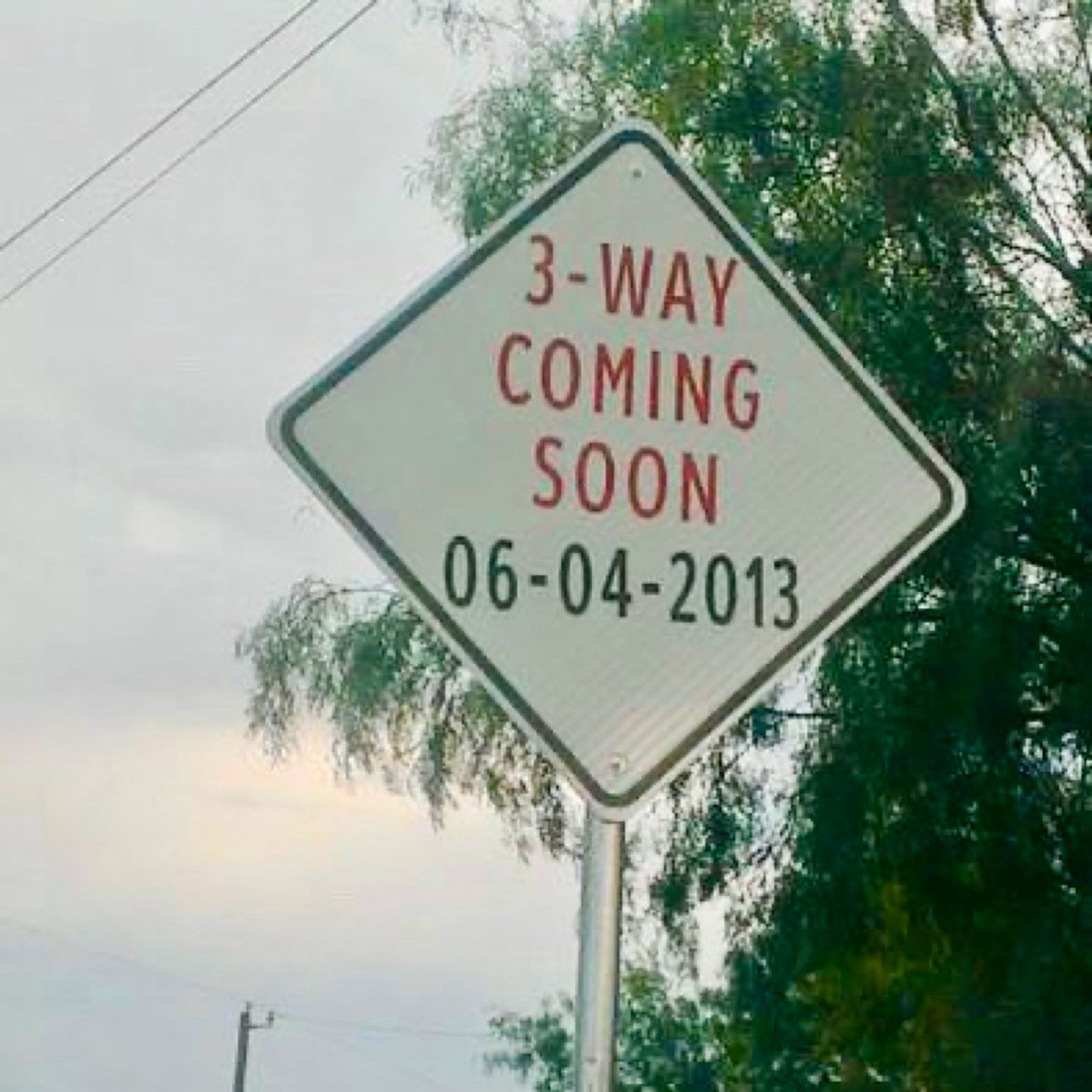 Street sign reads “3-WAY COMING SOON 06-04-2013.”