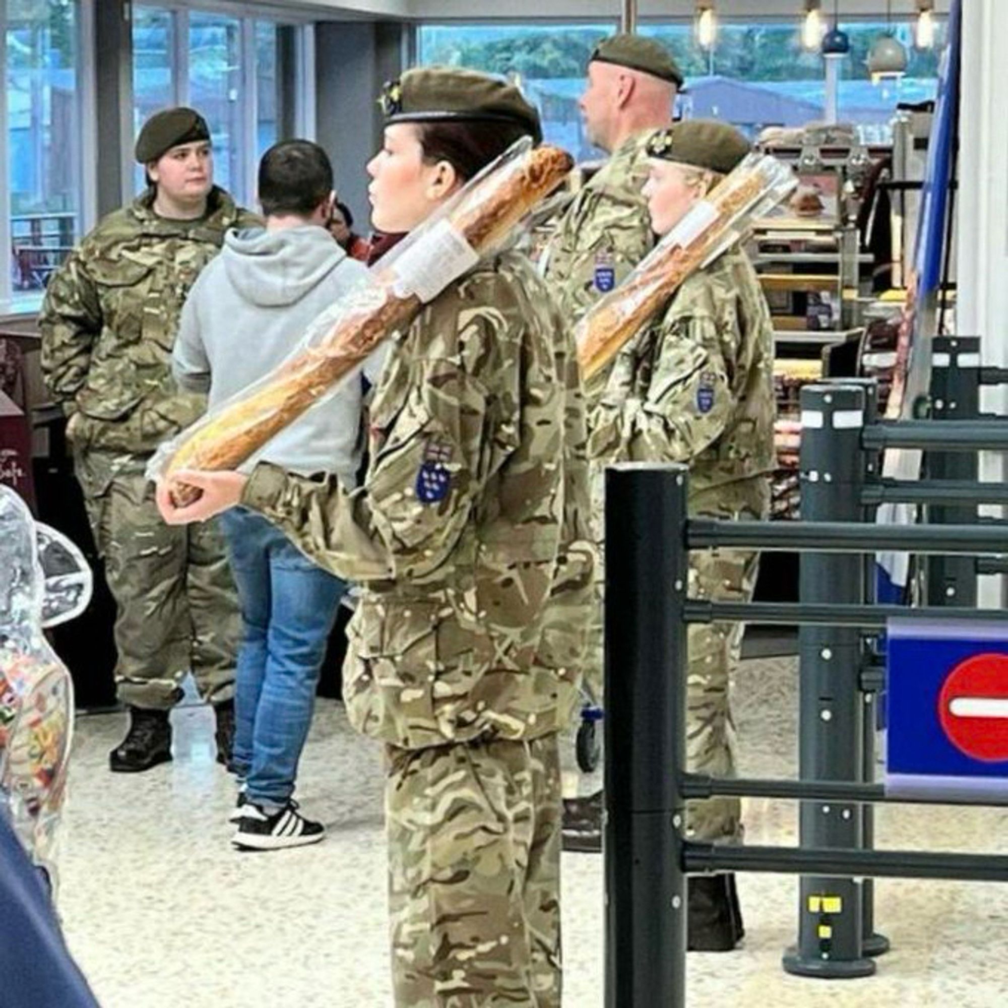 Soldiers lined up indoors at attention, holding baguettes on their shoulders like rifles.