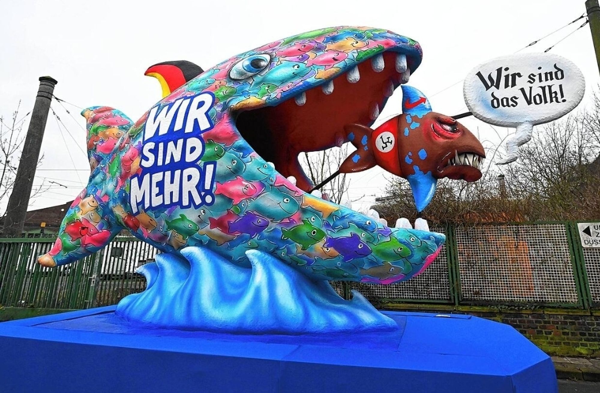 Motivwagen von Jacques Tilly zum Düsseldorfer Rosenmontagsumzug.
Ein kleiner Nazi Fisch mit Wir sind das Volk Sprechblase wird von einem riesigen Wir sind mehr Fisch gefressen.