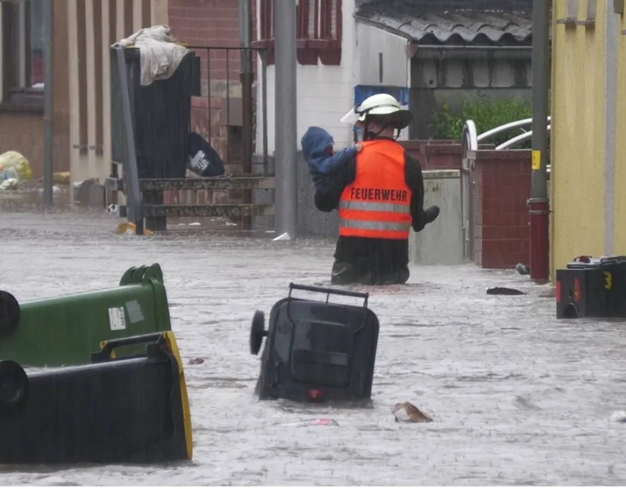 Ein Feuerwehrnann, der durch die Wassermassen läuft, in seinen Armen trägt er ein kleines Kind. Das Bild stammt aus dem Saarland von gestern.