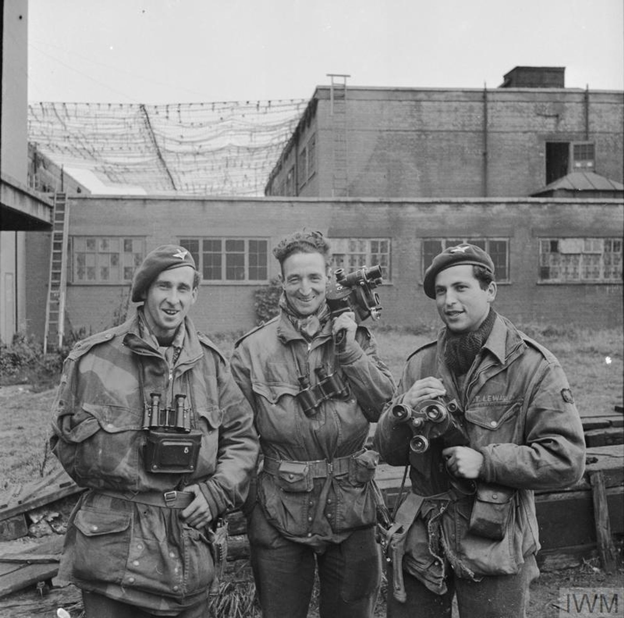 A black and white photograph of three men in military uniform. Two are holding cine cameras. IWM collections BU 1169